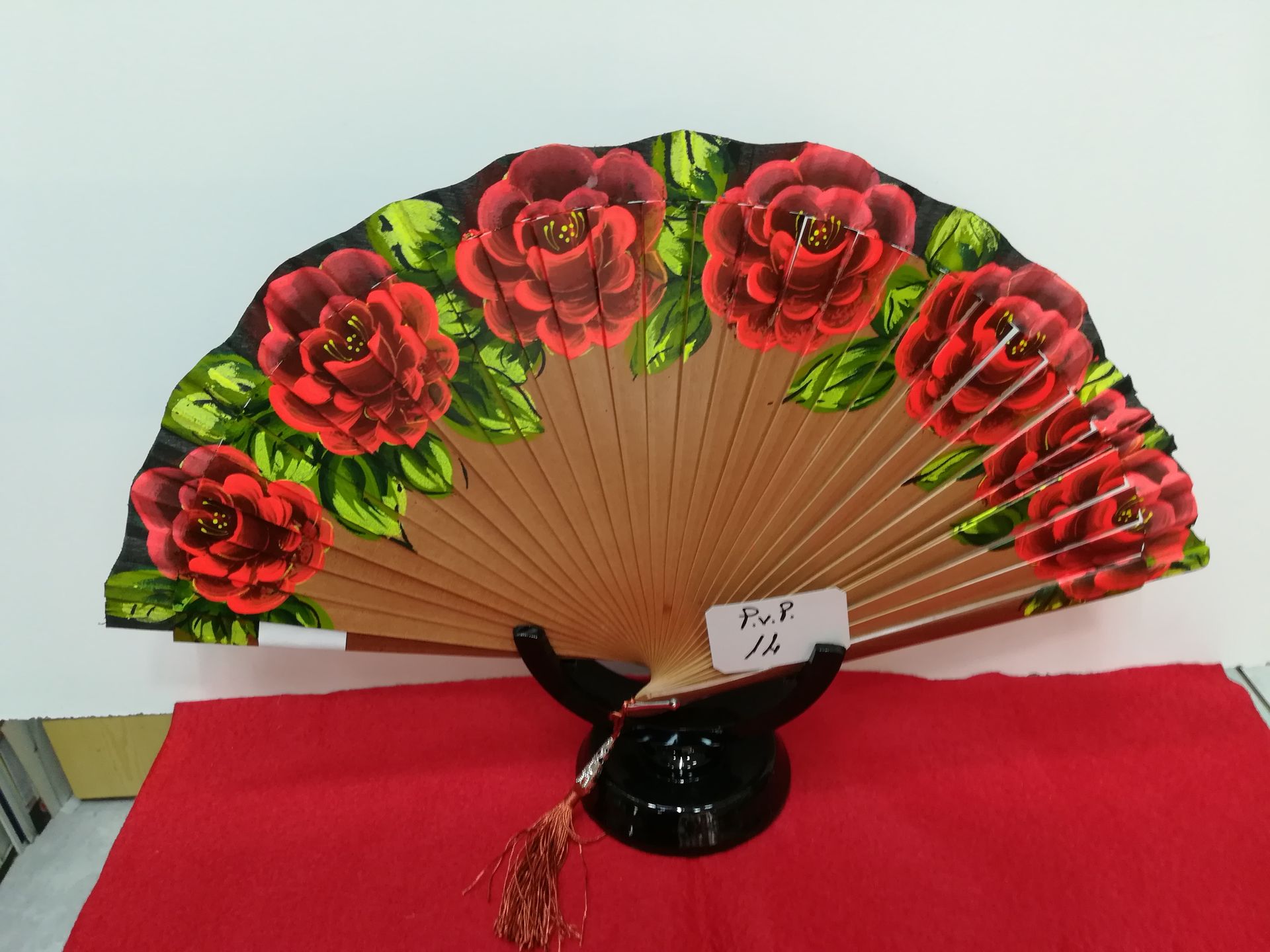 Un abanico con rosas rojas reposa sobre un paño rojo.