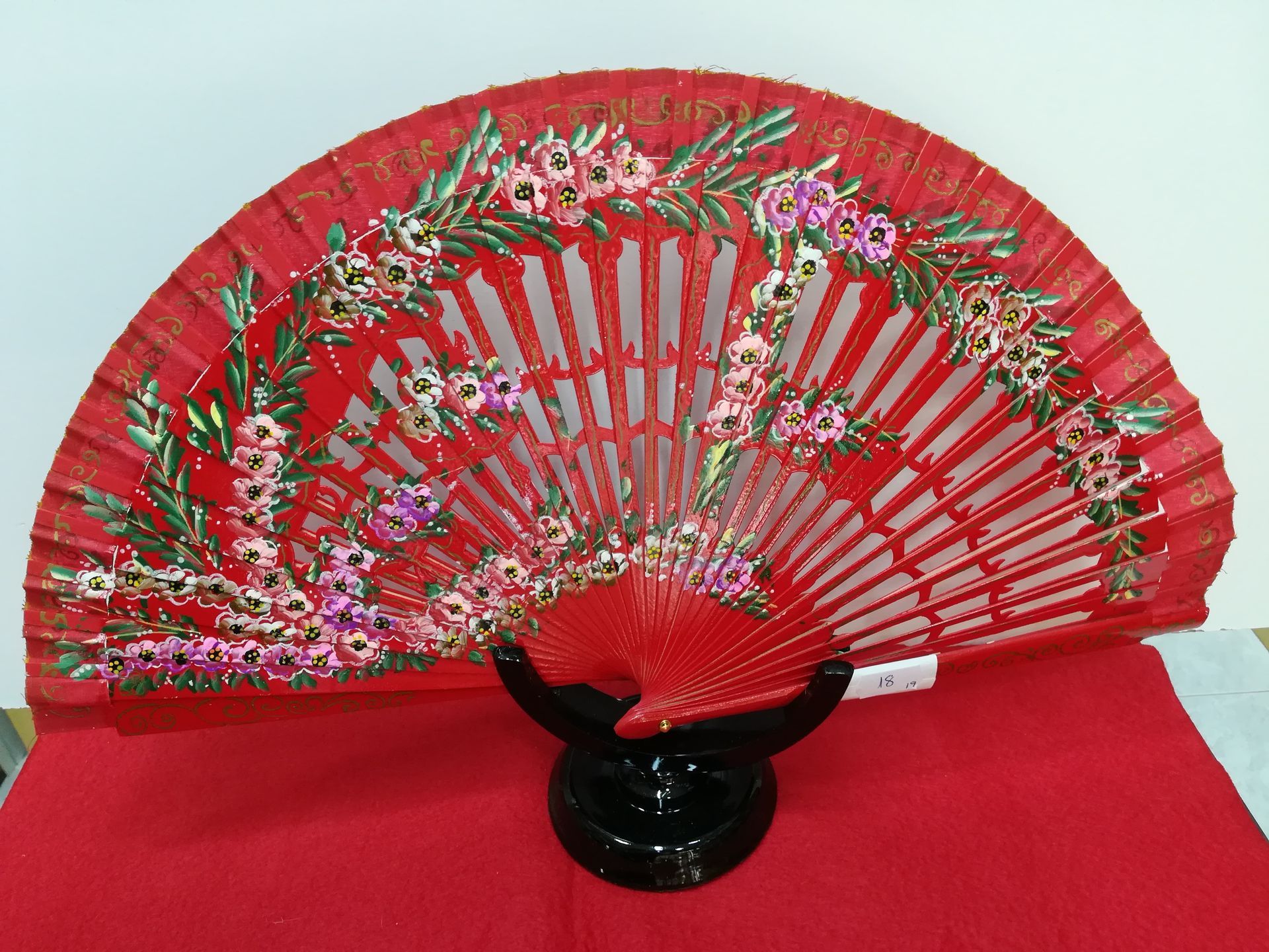 Un abanico rojo con flores está sobre un paño rojo.