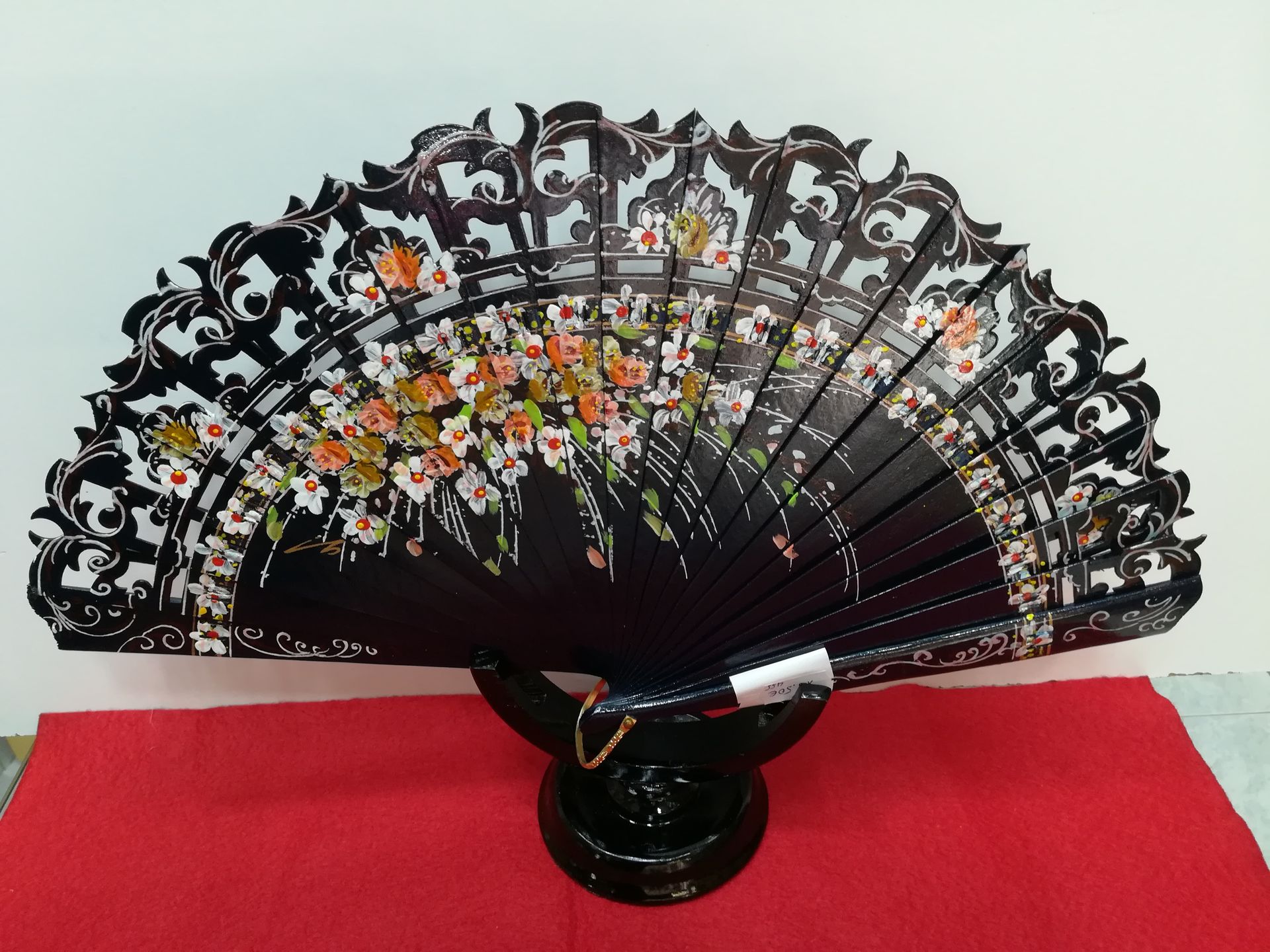 Un abanico negro con flores está sobre una mesa roja.