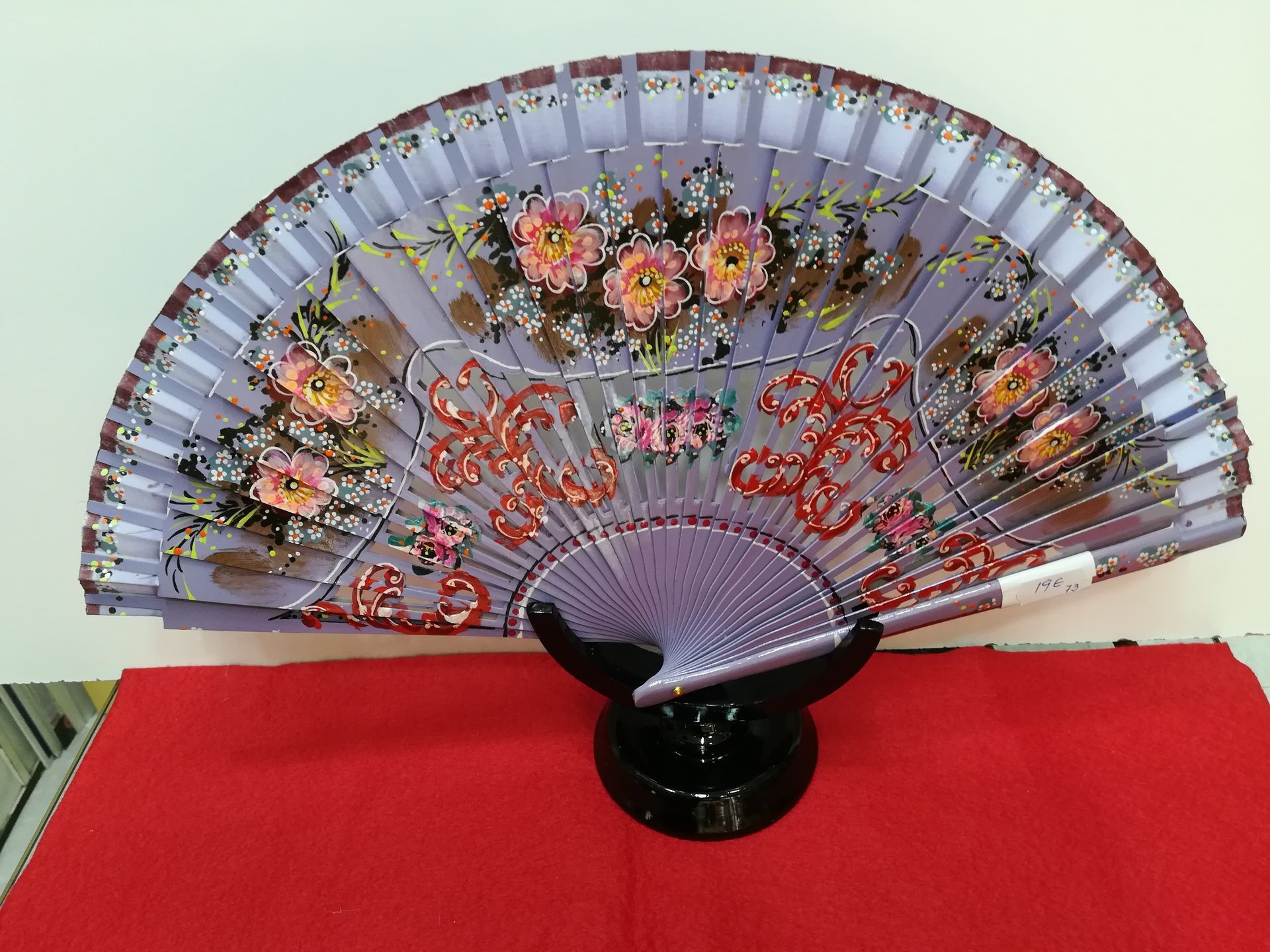 Un abanico morado con flores reposa sobre una tela roja.