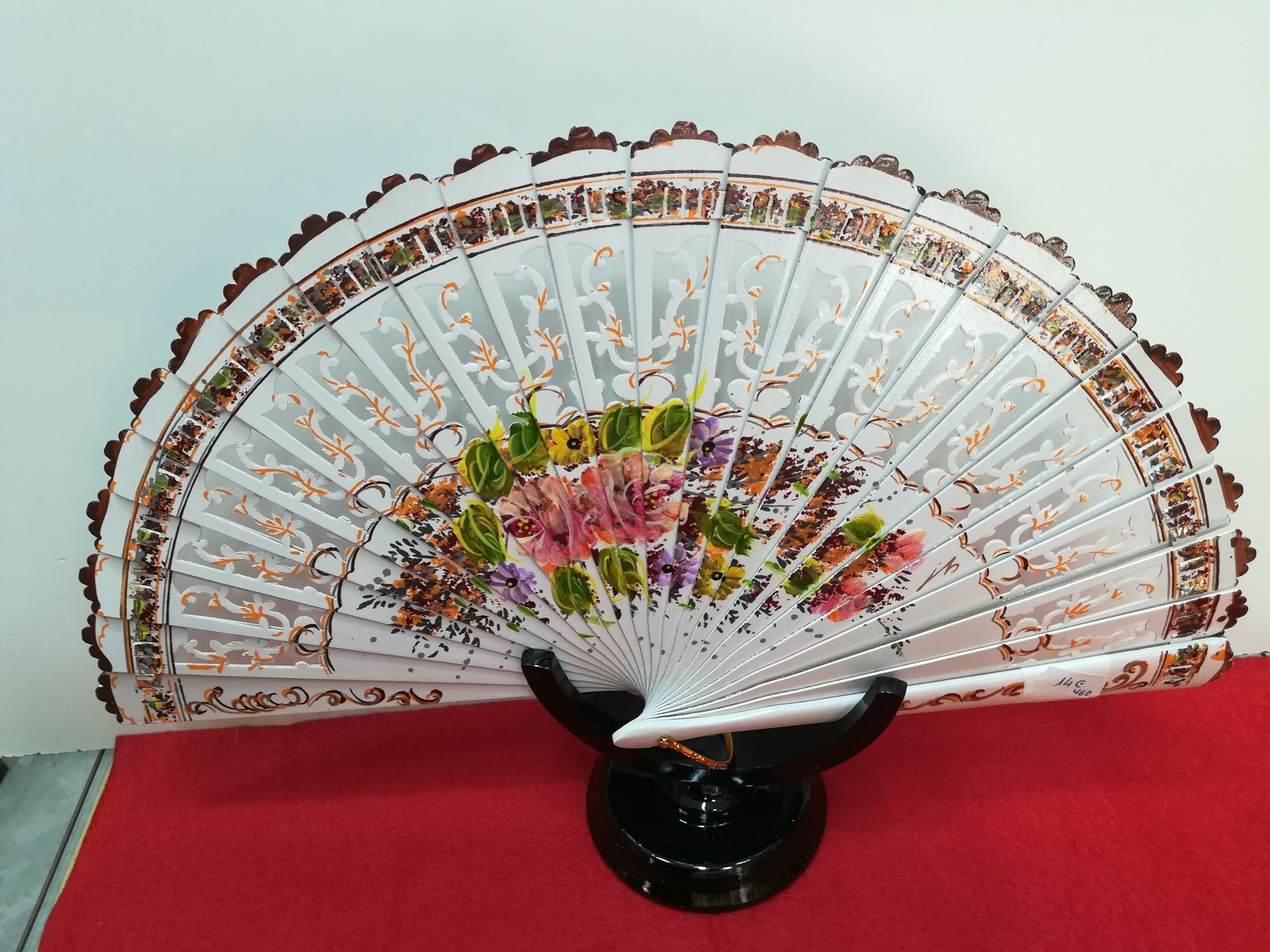 Un abanico blanco con flores está sobre un soporte negro.