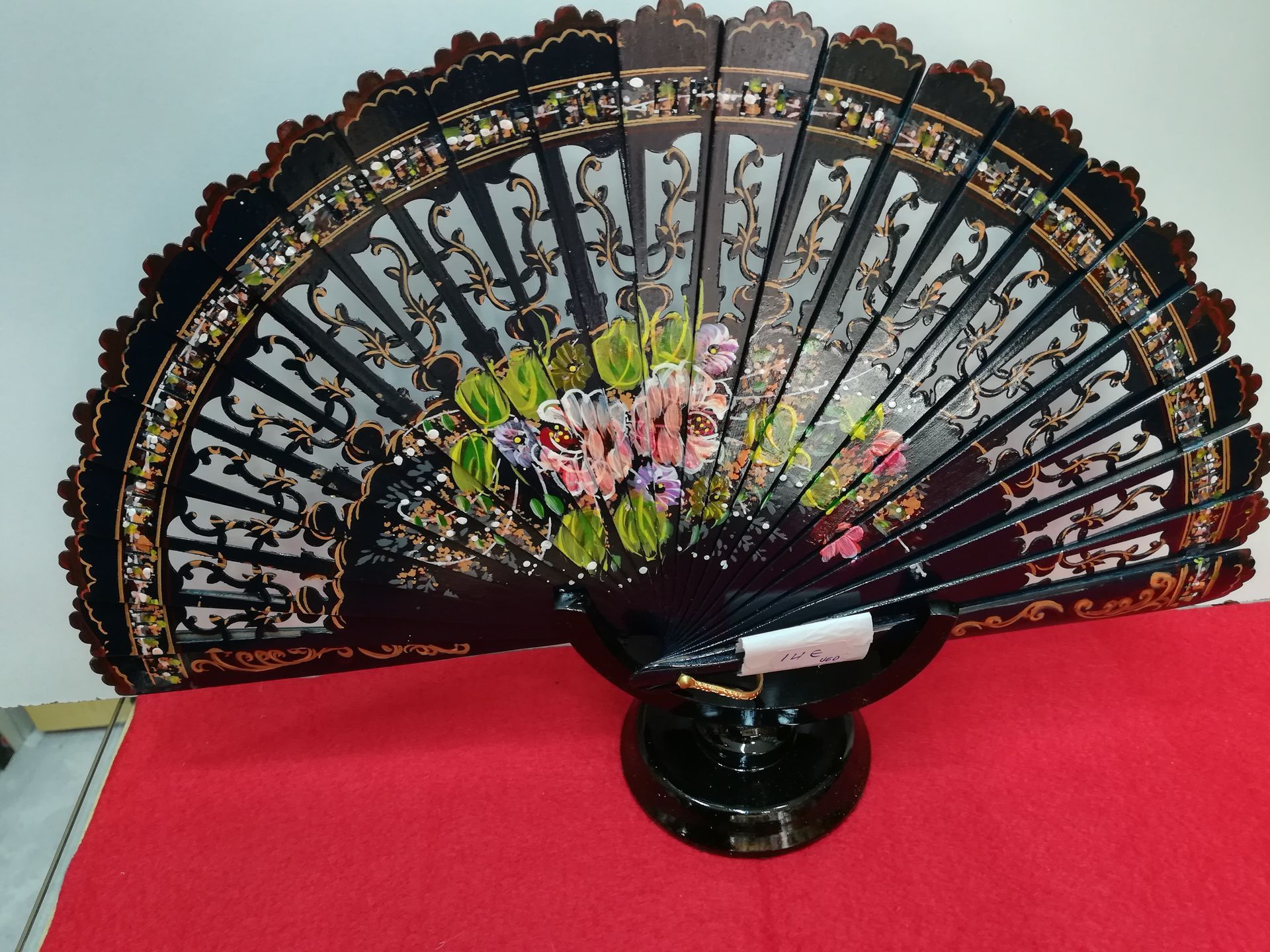 Un abanico negro con flores reposa sobre una mesa roja.