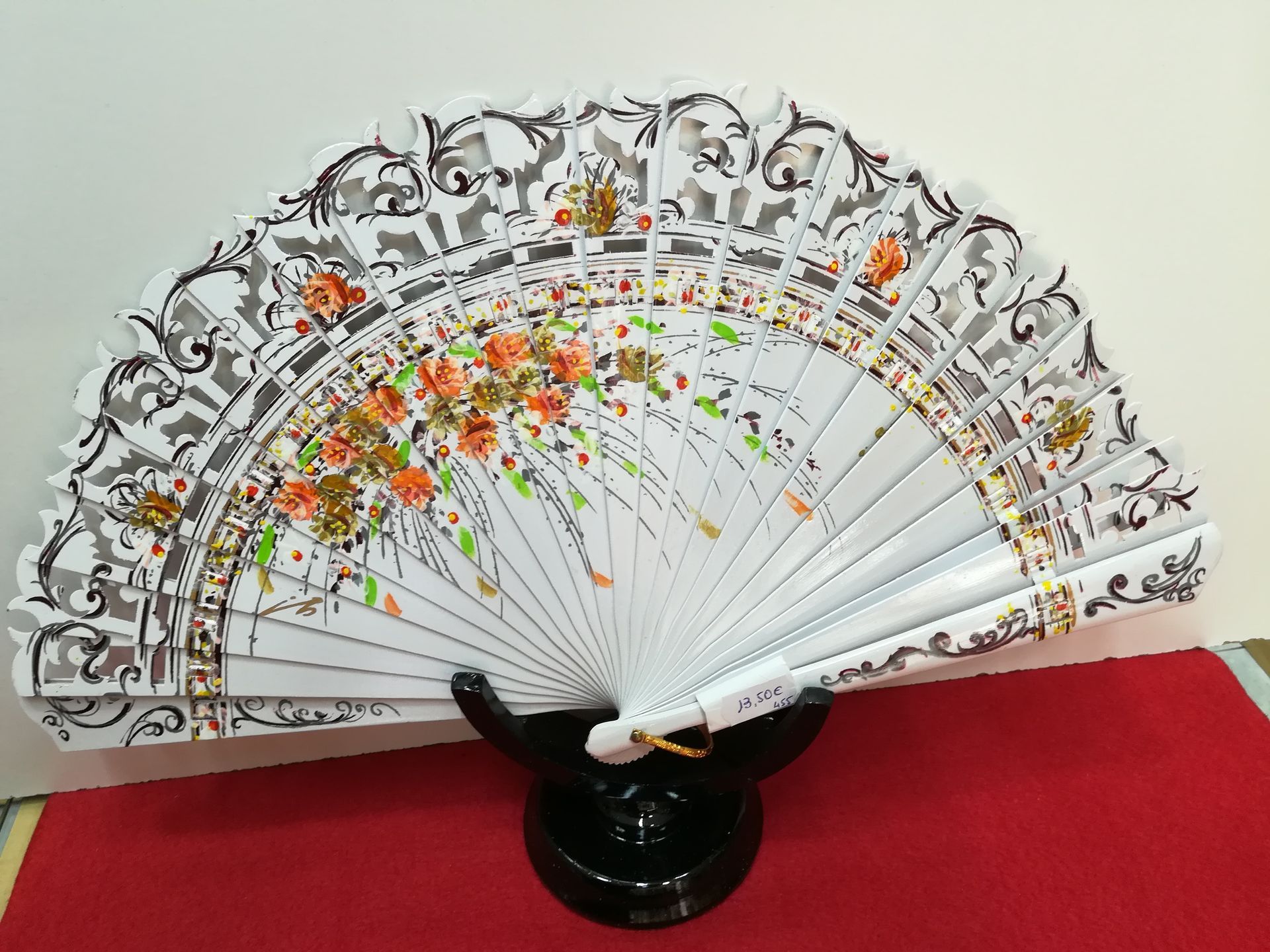 Un abanico blanco con flores está sobre una mesa roja.