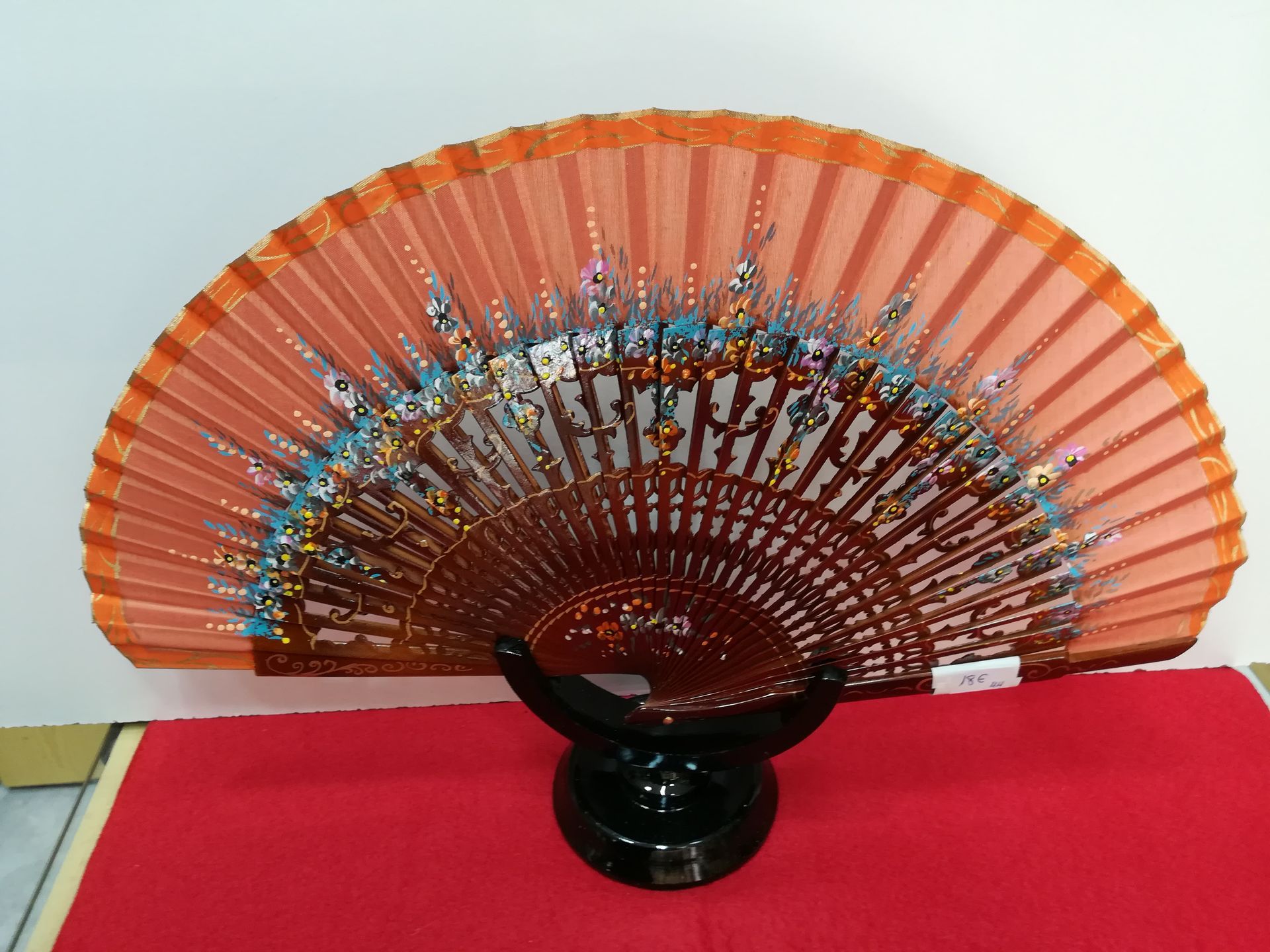 Un abanico naranja está sentado encima de una tela roja.