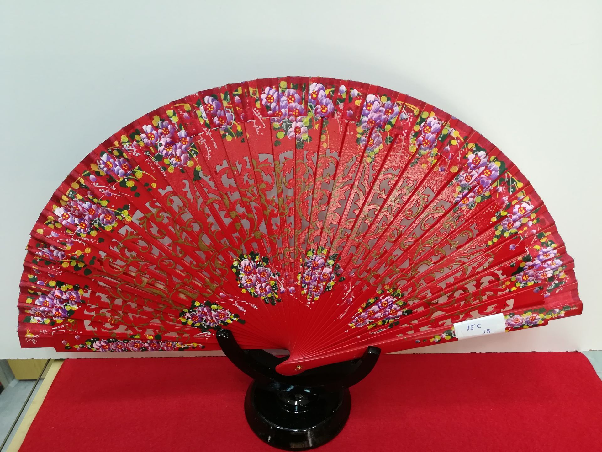 Un abanico rojo con flores está sobre un soporte negro.