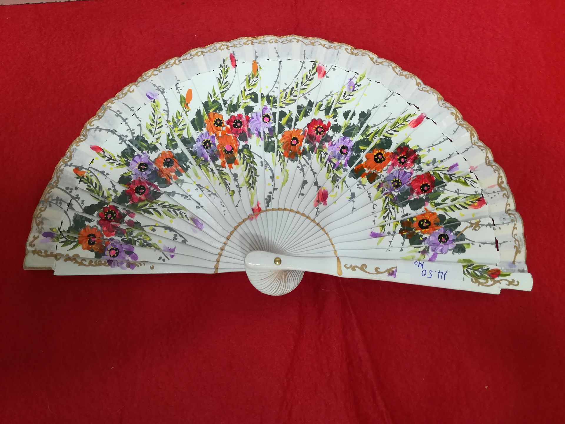 Un abanico blanco con flores pintadas está sobre una tela roja.