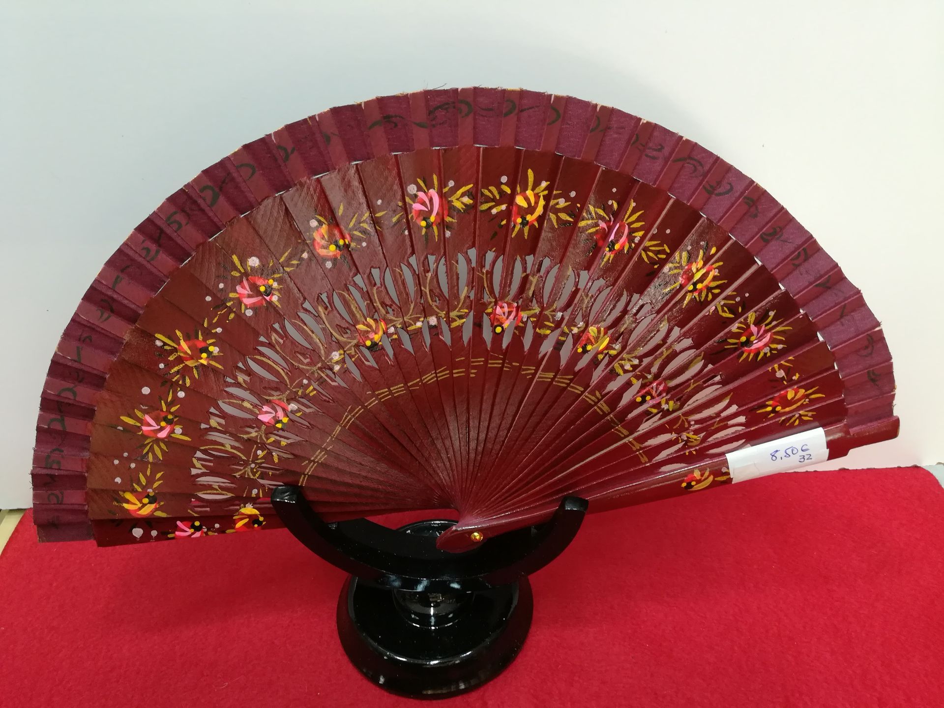 Un abanico rojo con flores está sobre un soporte negro.