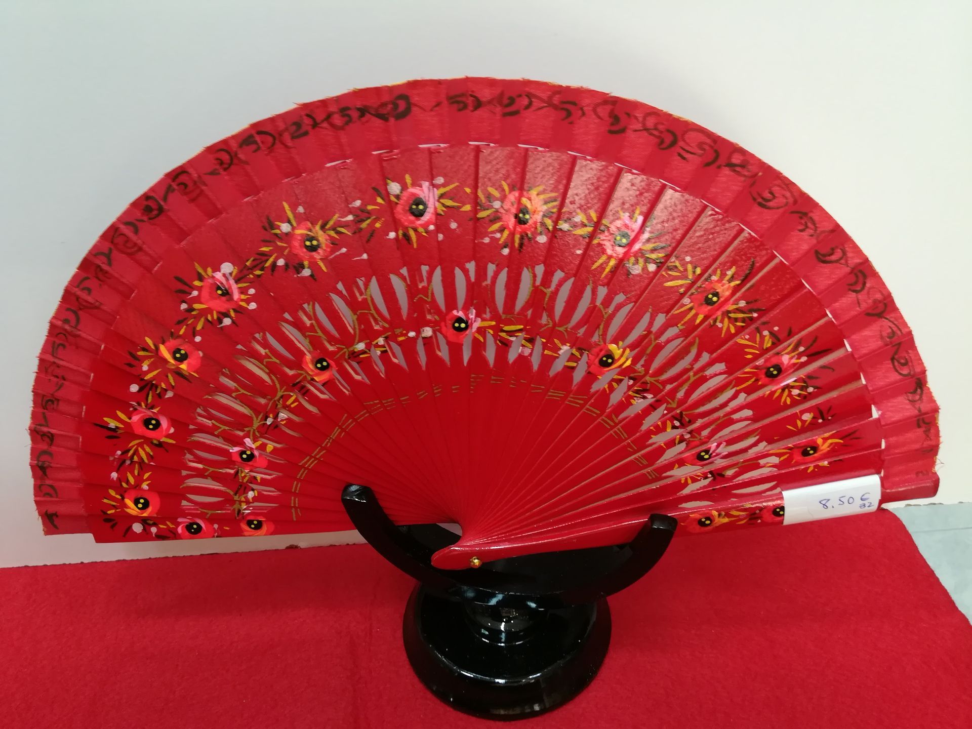 Un abanico rojo con flores reposa sobre un soporte negro.