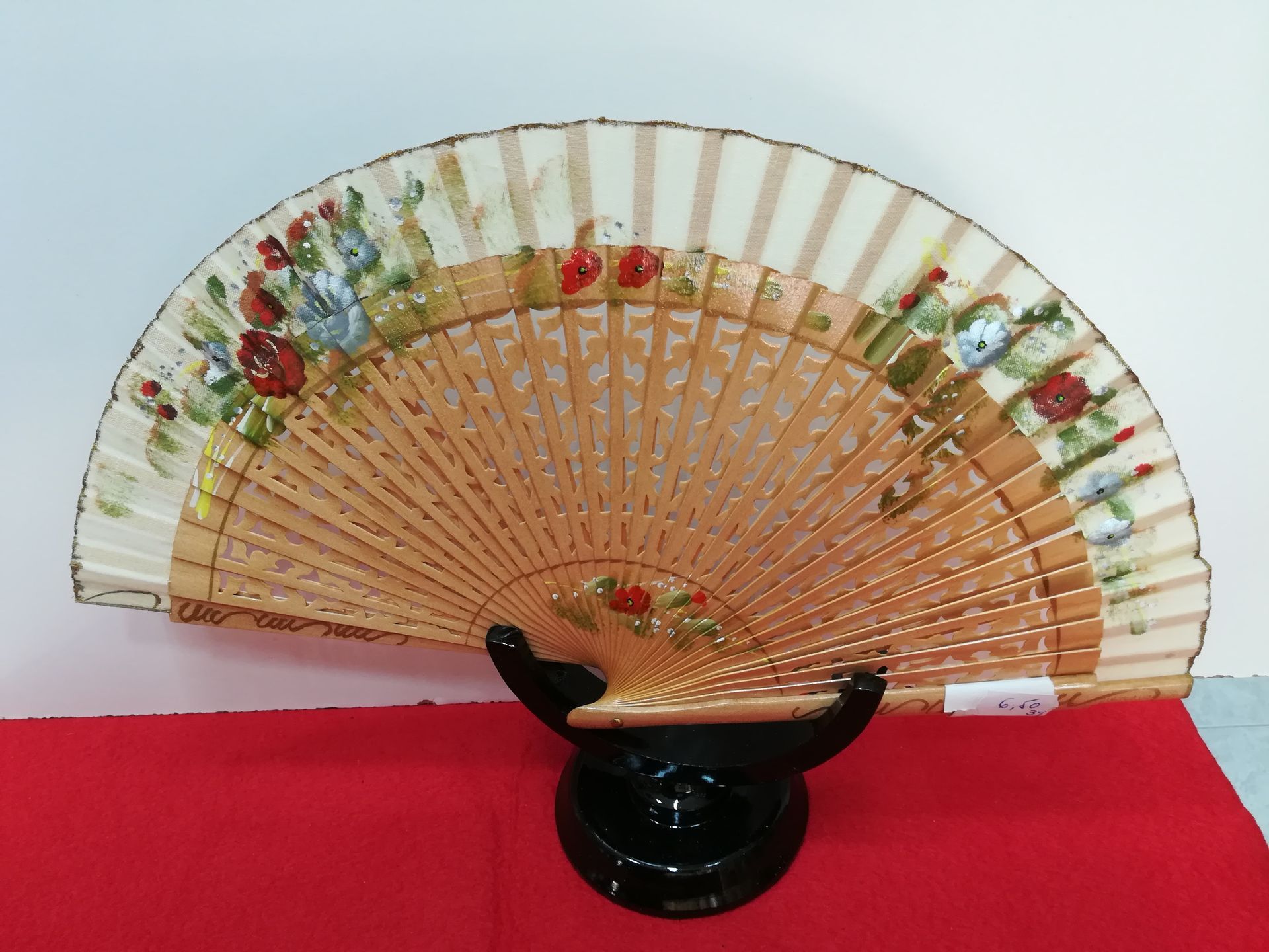 Un abanico con flores pintadas reposa sobre una tela roja.