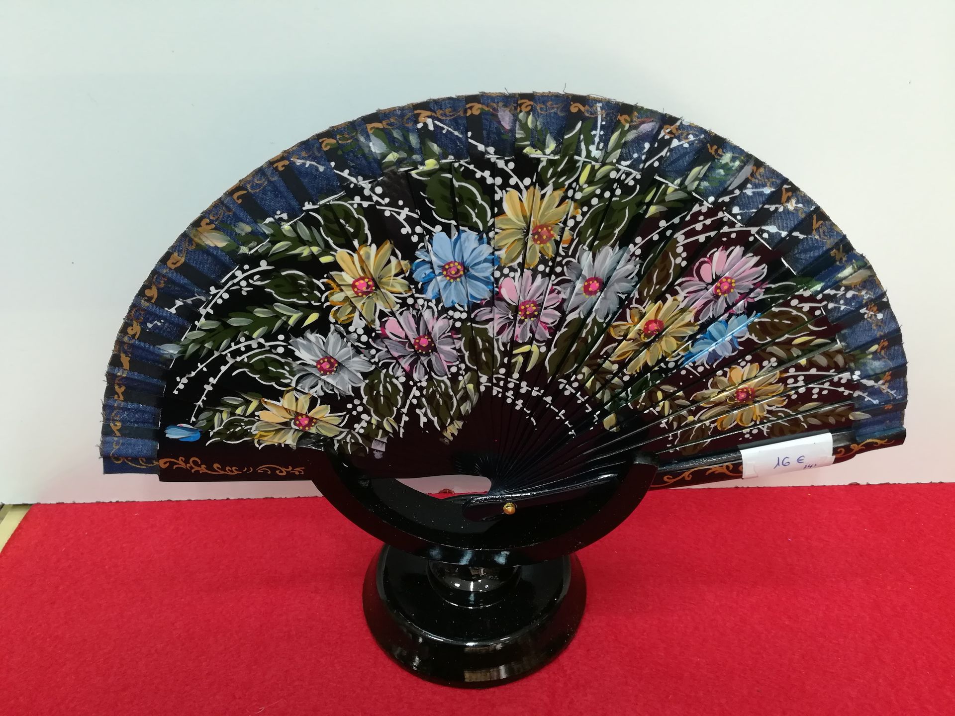 Un abanico con flores pintadas está sobre un soporte.