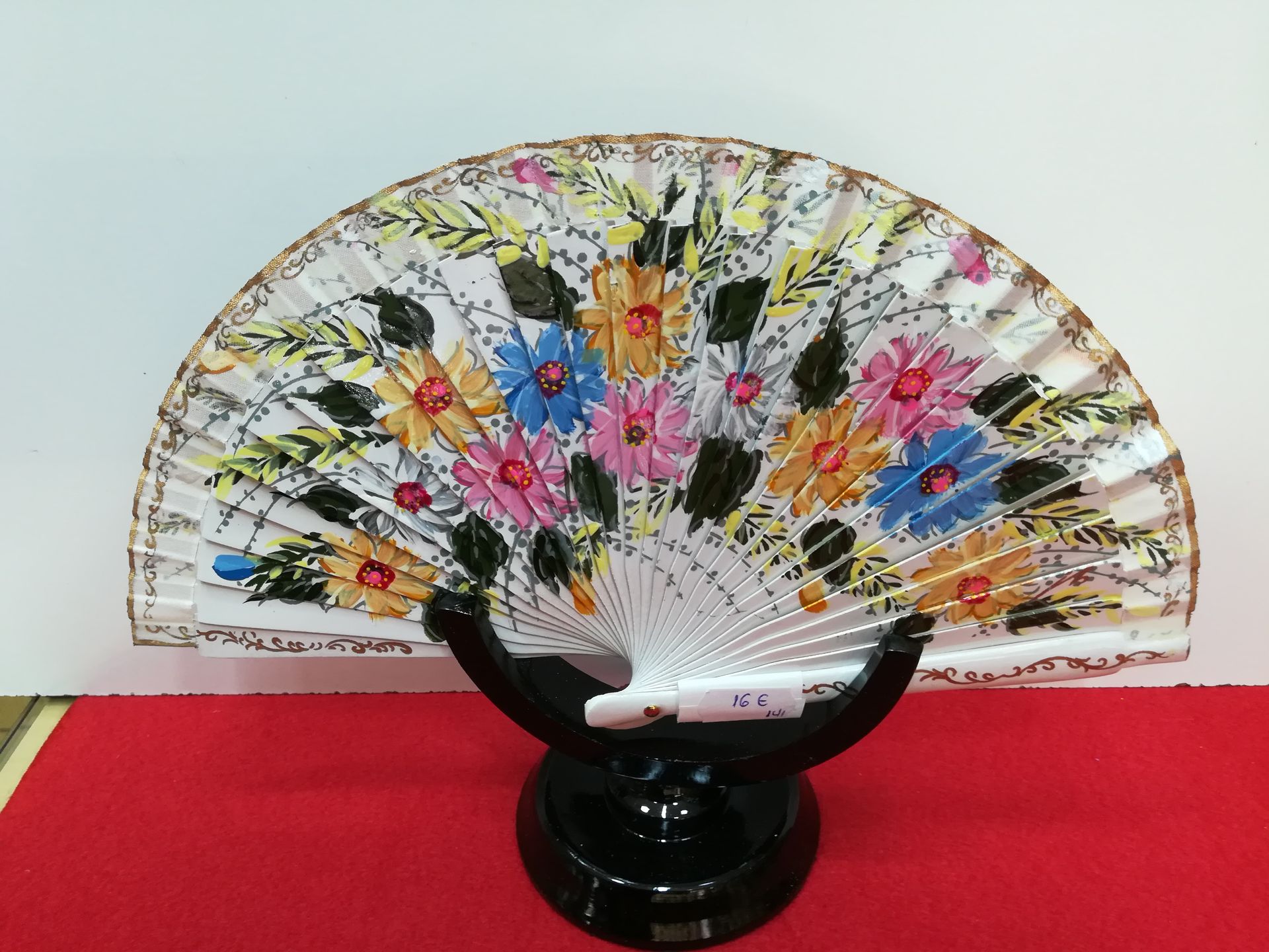 Un abanico con flores pintadas se encuentra sobre un soporte negro.