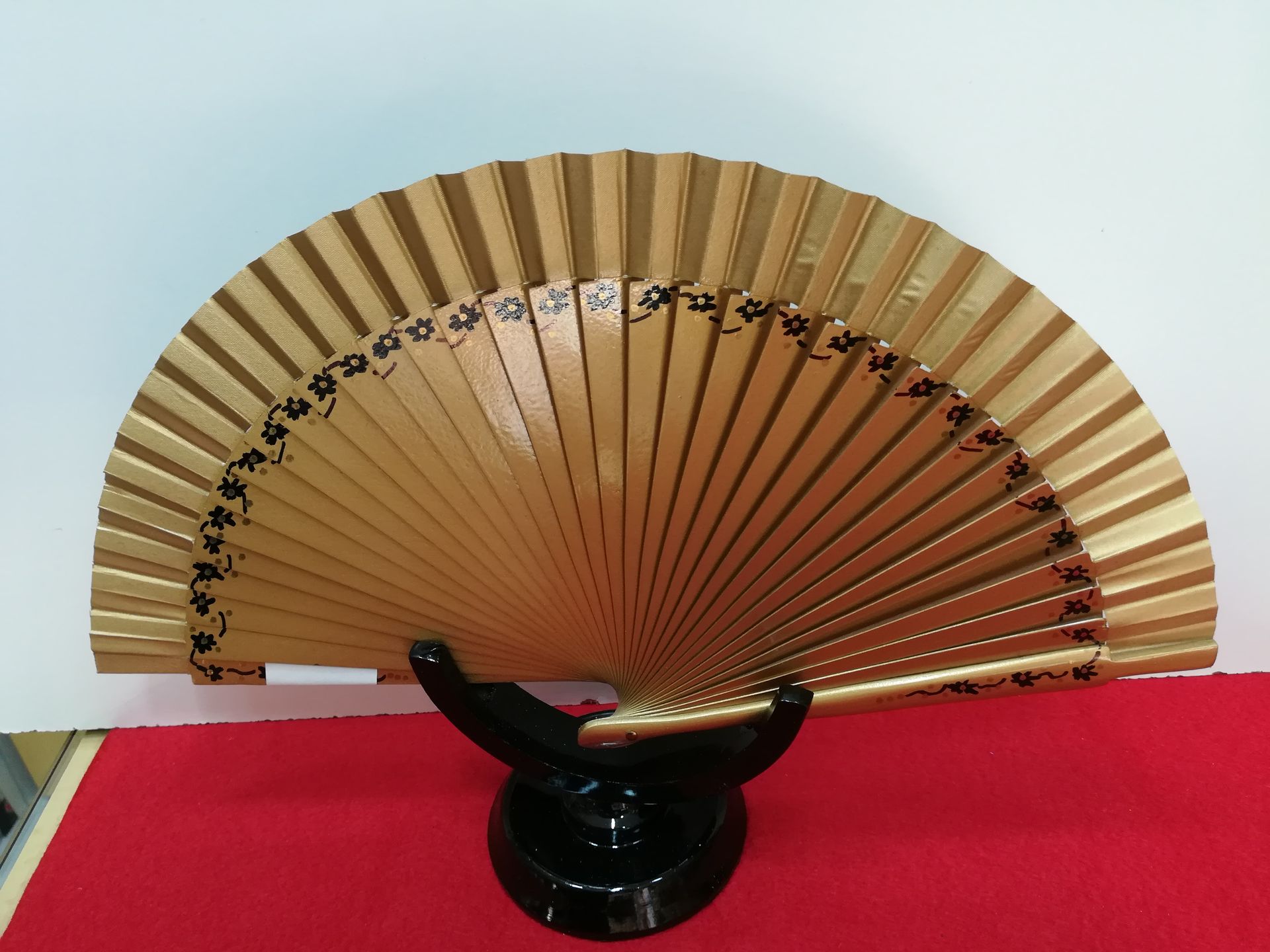 Un abanico dorado está sentado sobre un soporte negro.