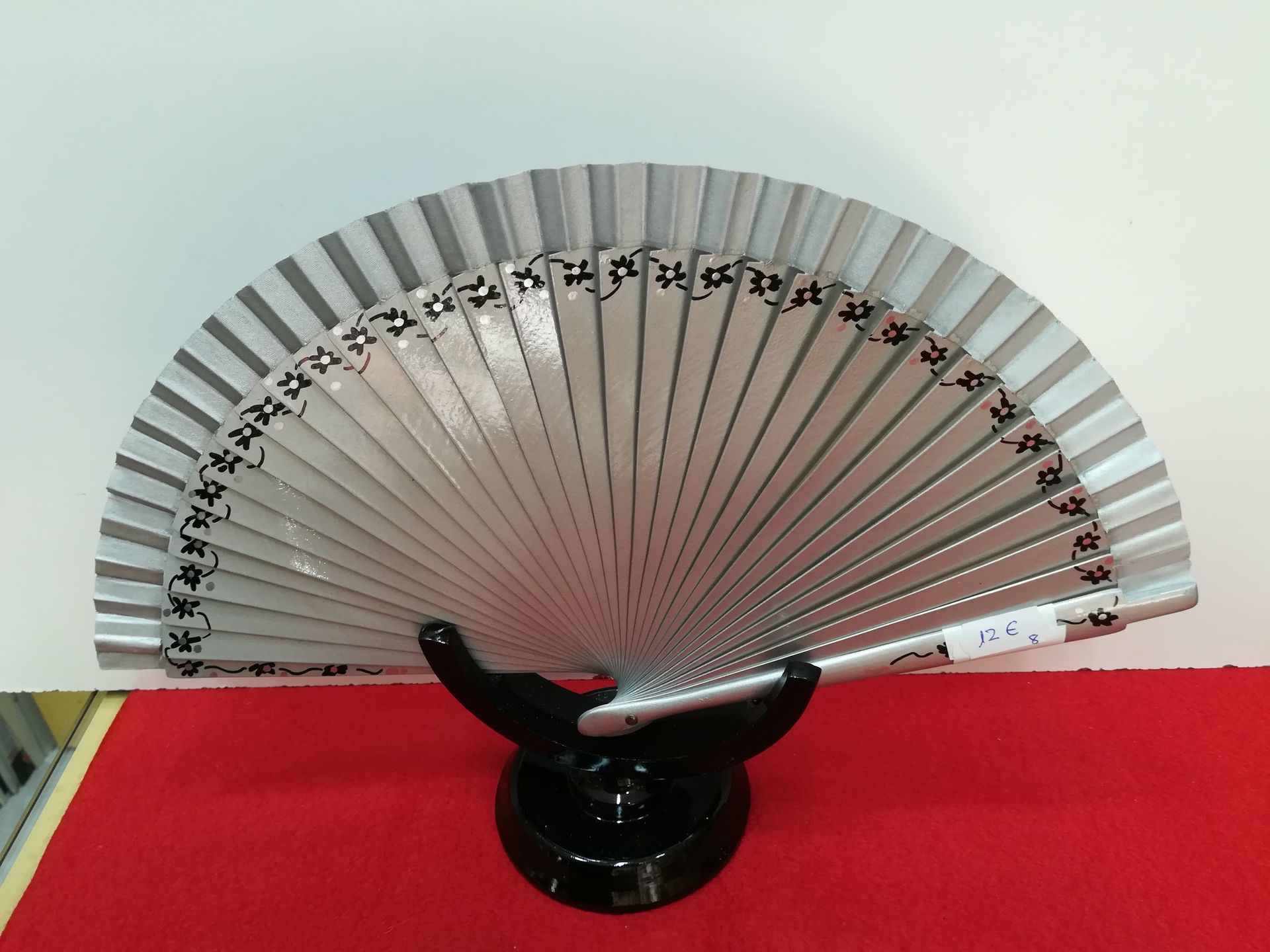 Un ventilador plateado está sentado sobre un soporte negro.