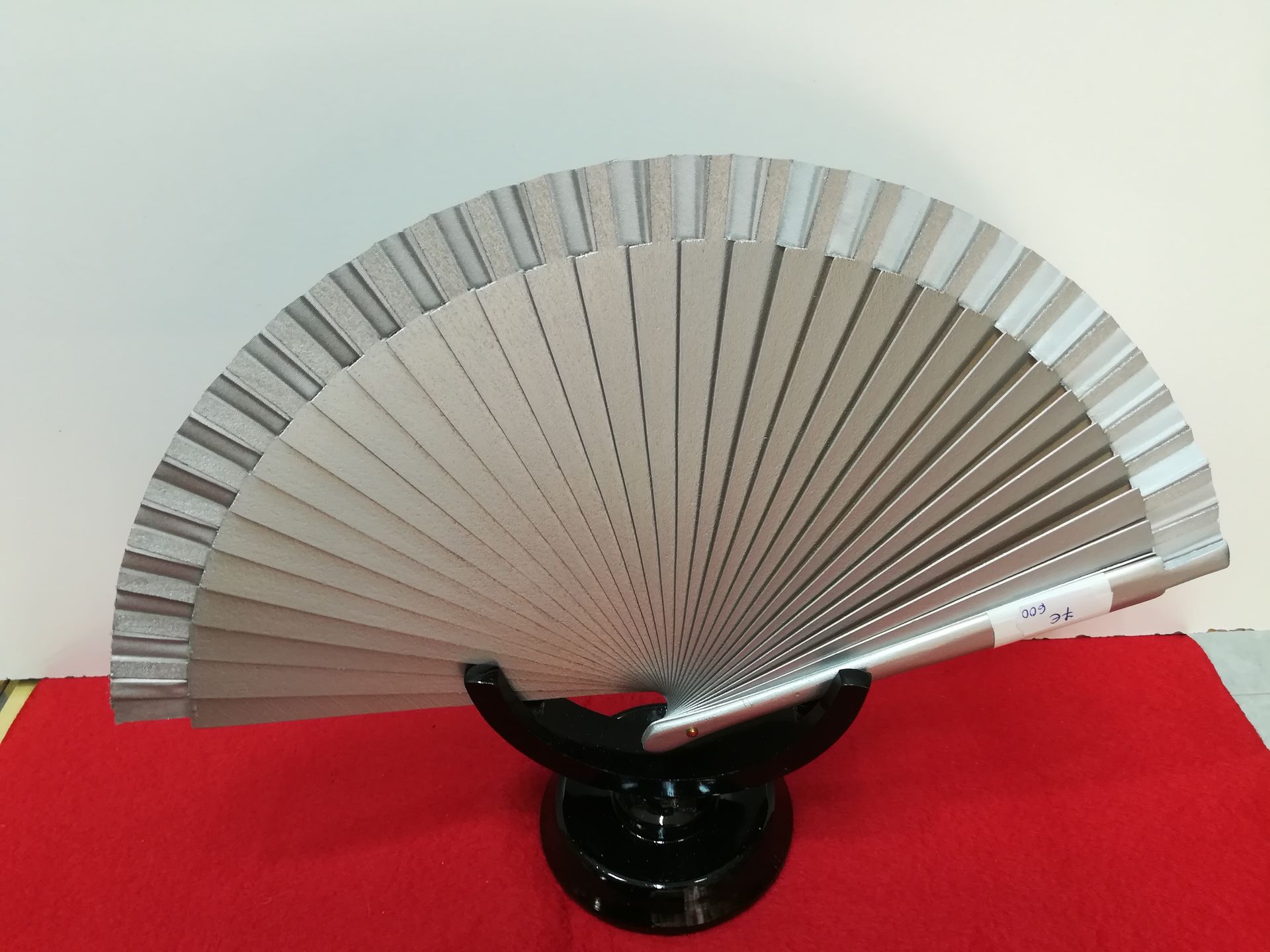 Un abanico plateado está sentado sobre un soporte negro sobre una tela roja.
