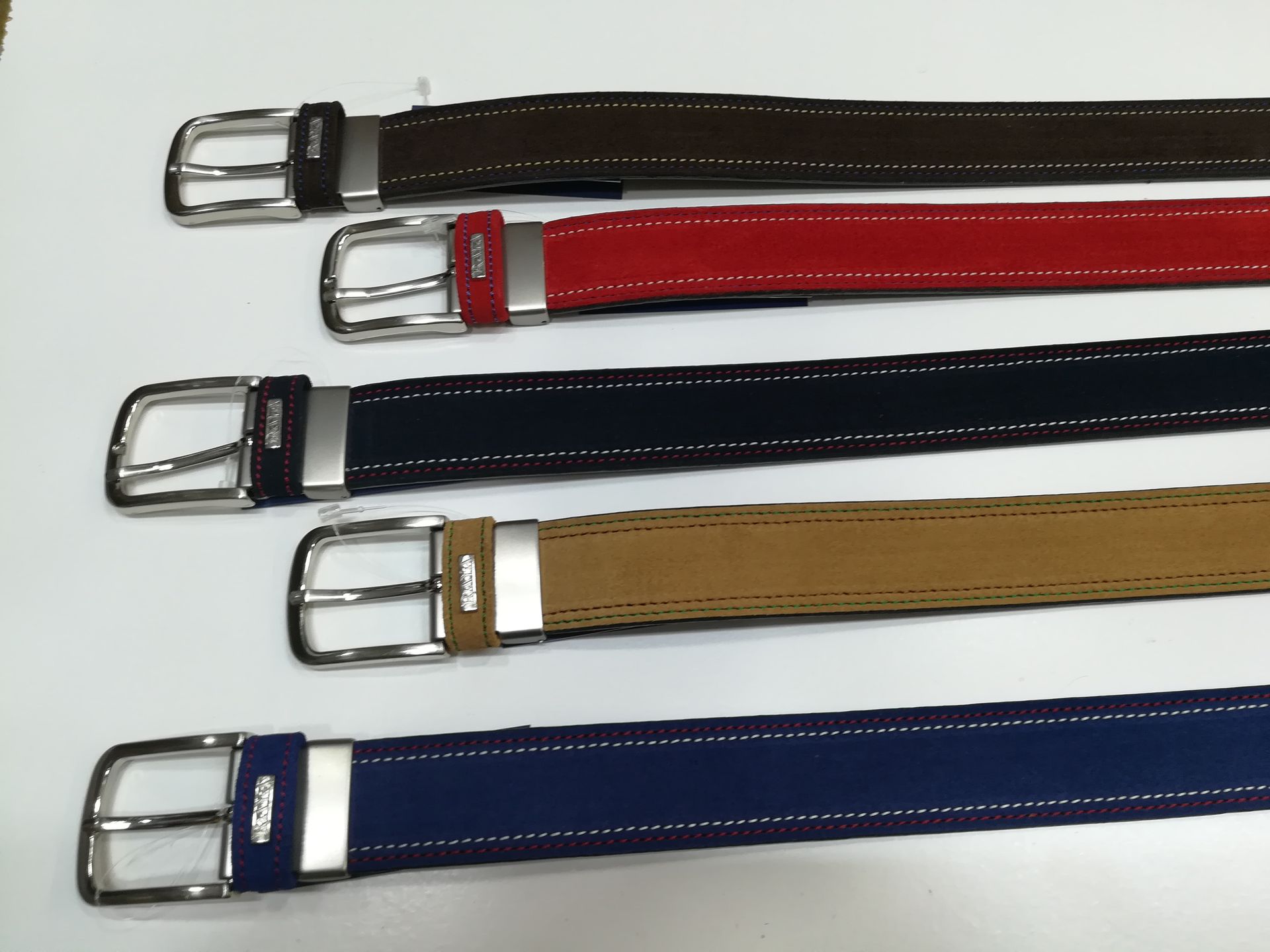 Cinco cinturones de diferentes colores están alineados sobre una superficie blanca