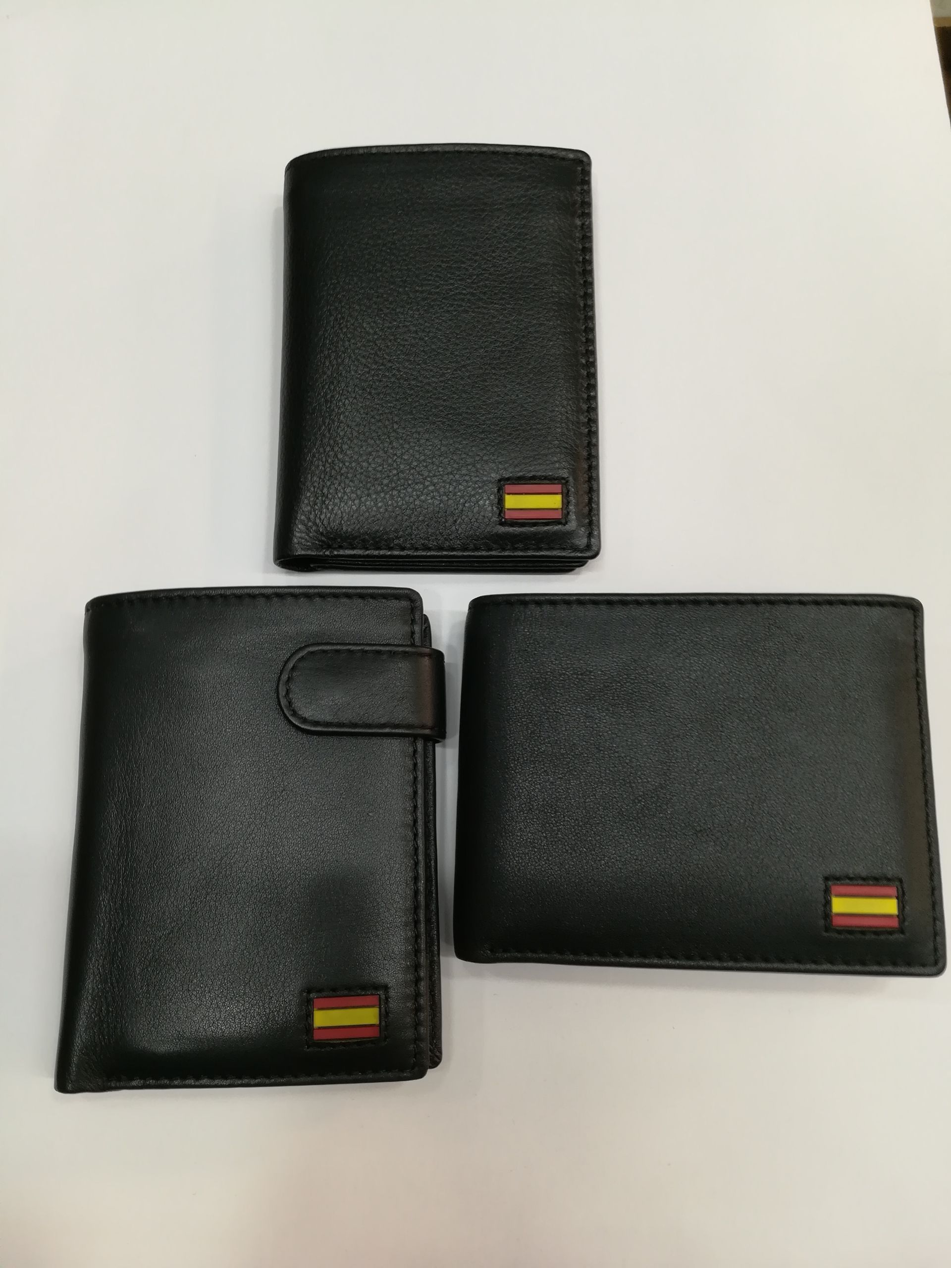 Tres carteras negras con banderas españolas están sobre una mesa blanca.