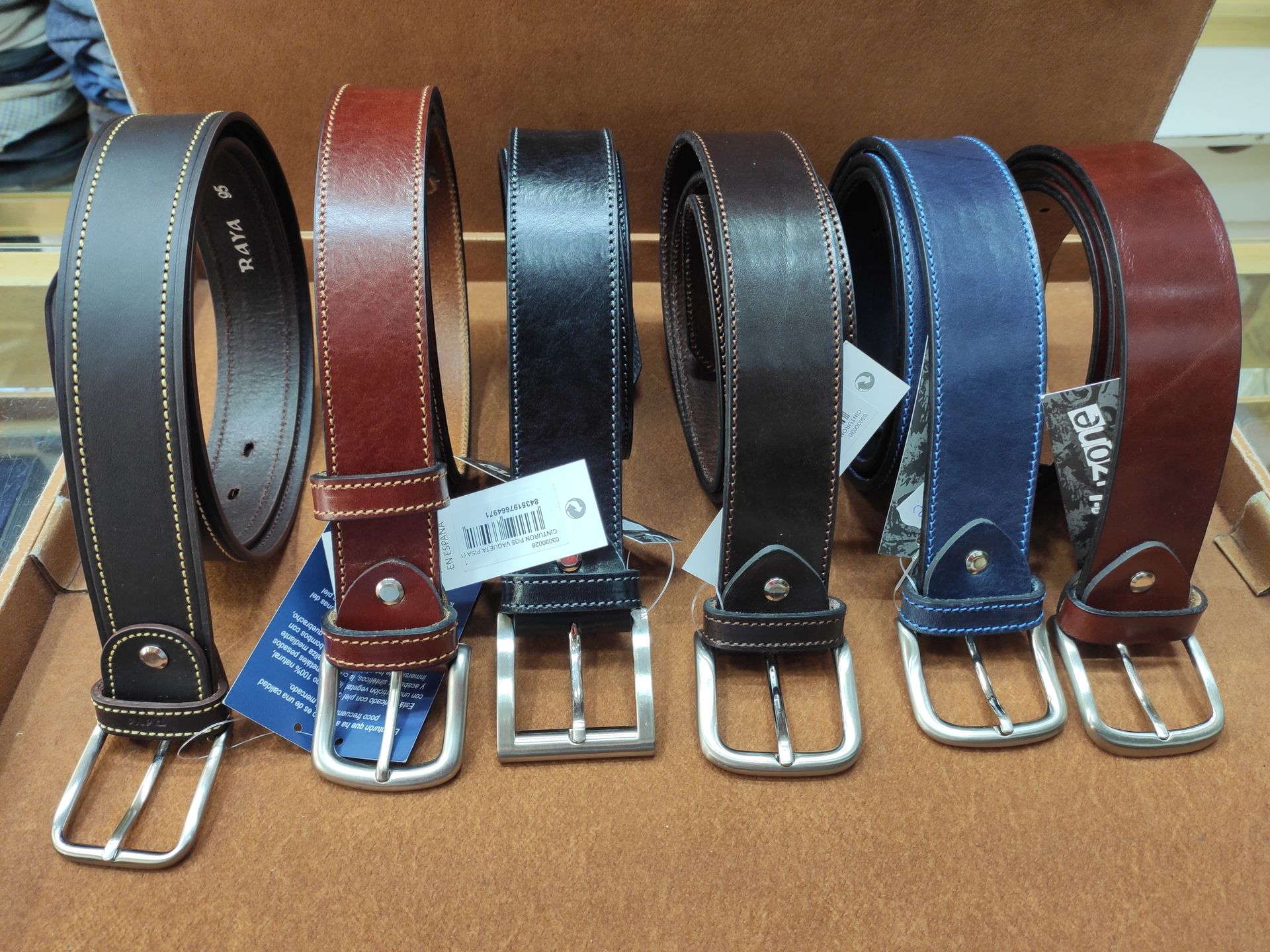 Varios cinturones de cuero de diferentes colores están alineados sobre una mesa.