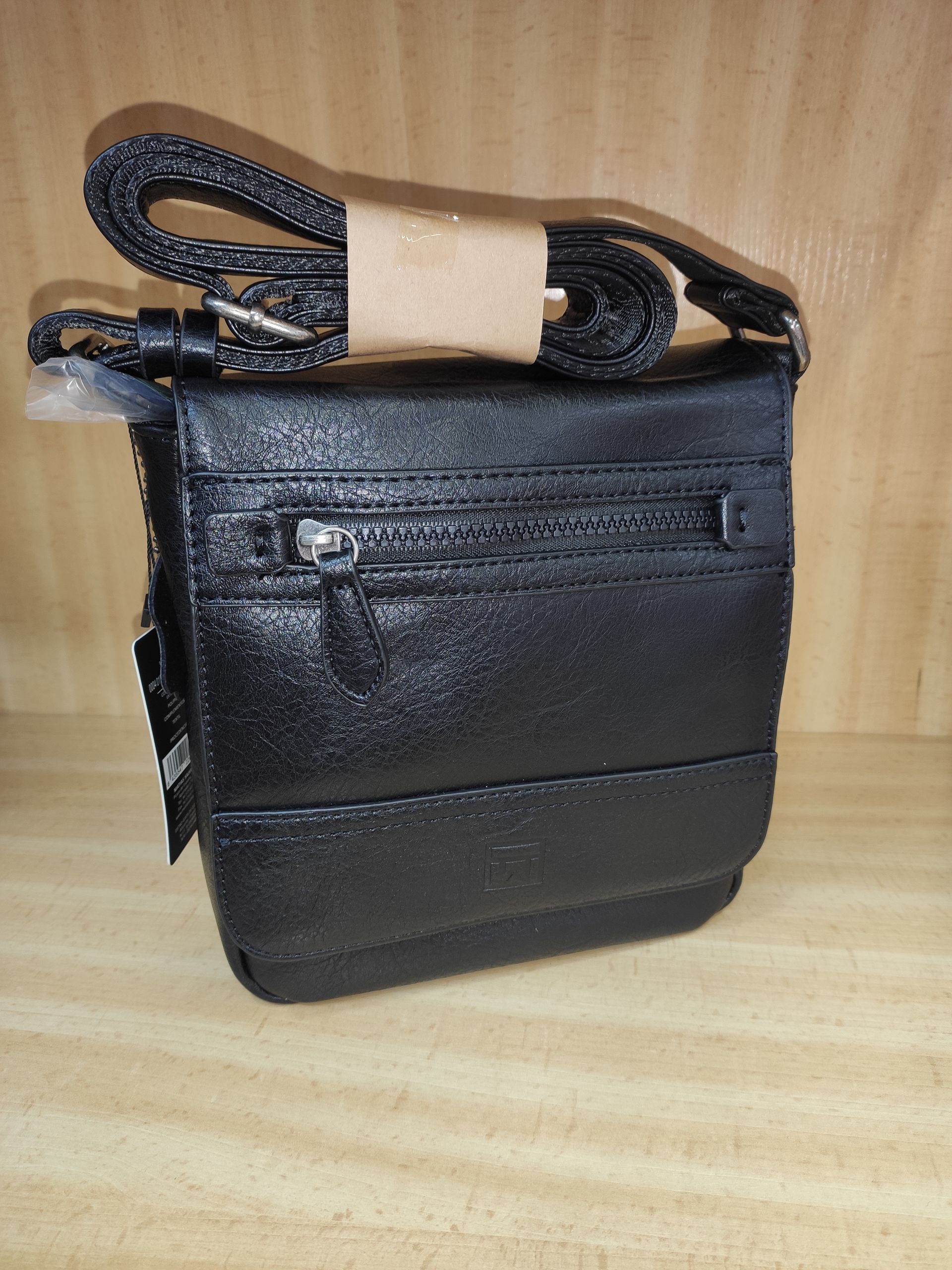 Un bolso negro con una correa está sobre una mesa de madera.