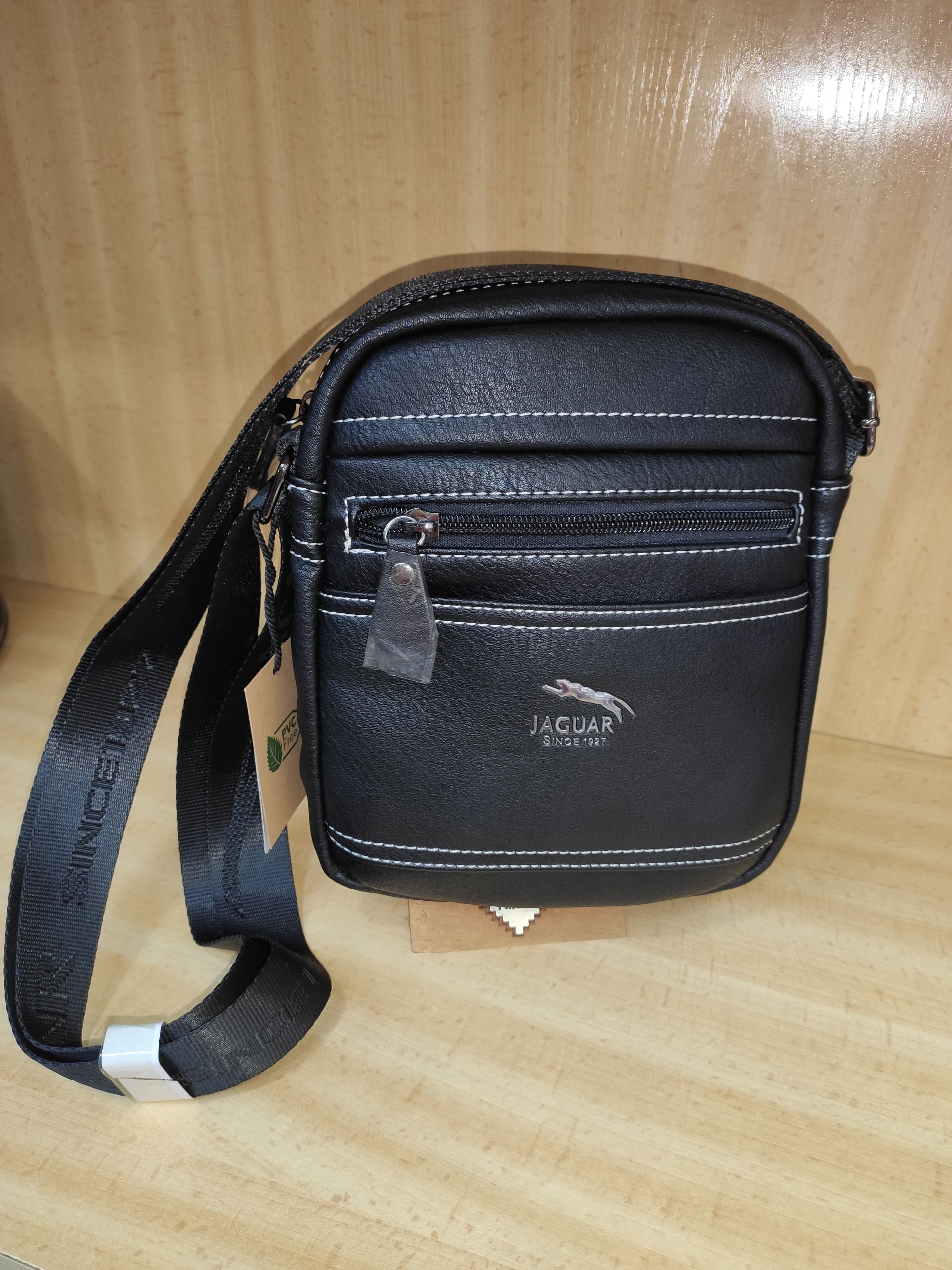 Un pequeño bolso negro con una correa está sobre un estante de madera.