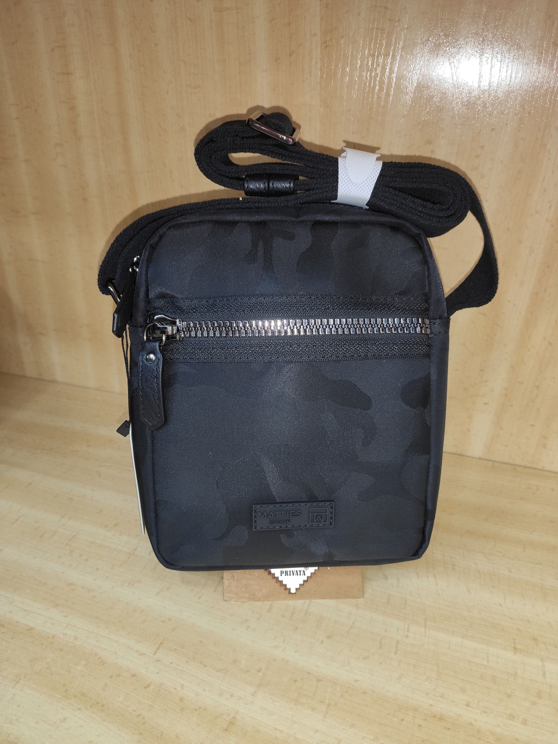 Un pequeño bolso negro con una correa está sobre una mesa de madera.