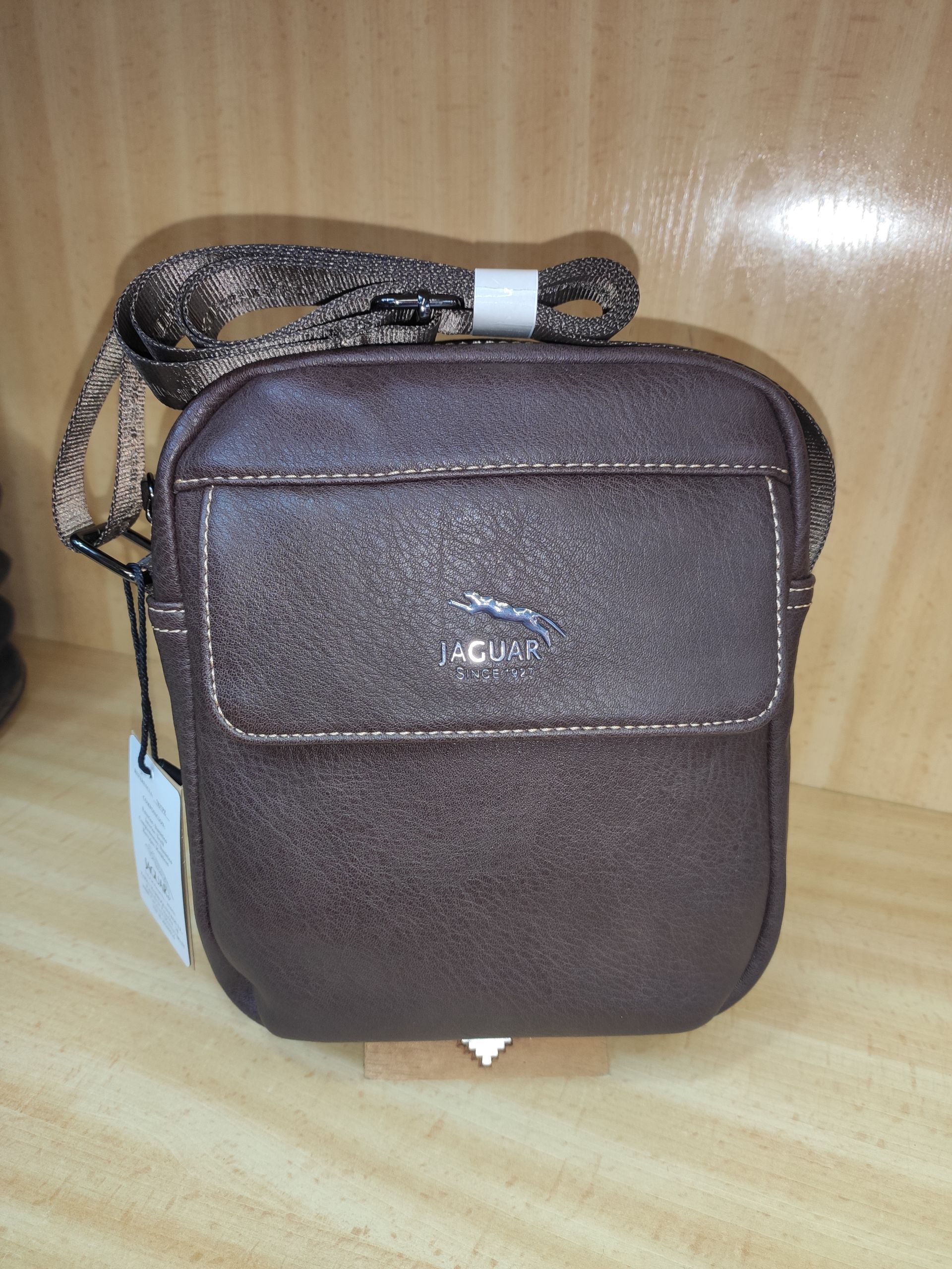 Una pequeña bolsa marrón con una correa está sobre una mesa de madera.