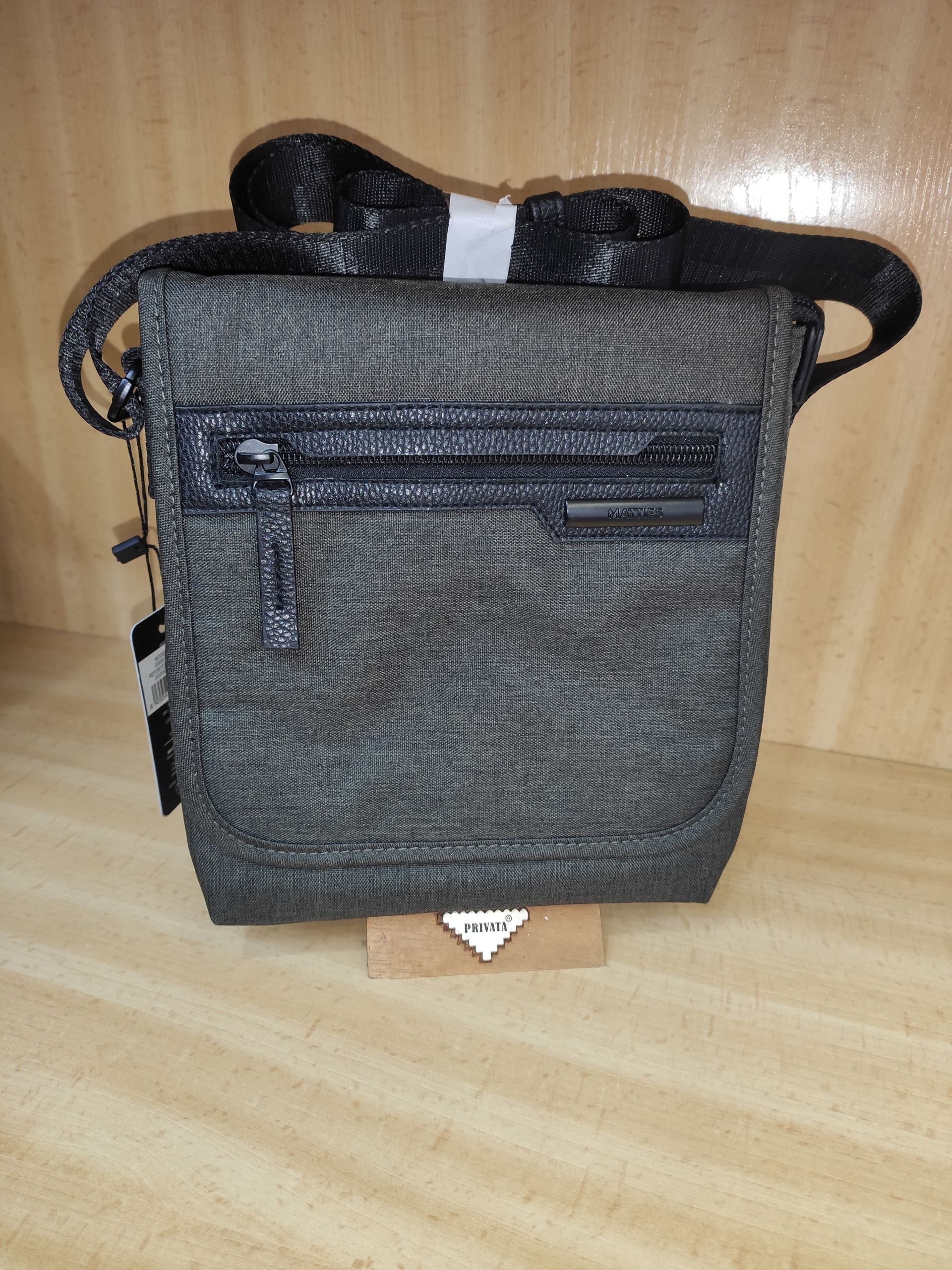 Un pequeño bolso gris con una correa negra está sobre una mesa de madera.