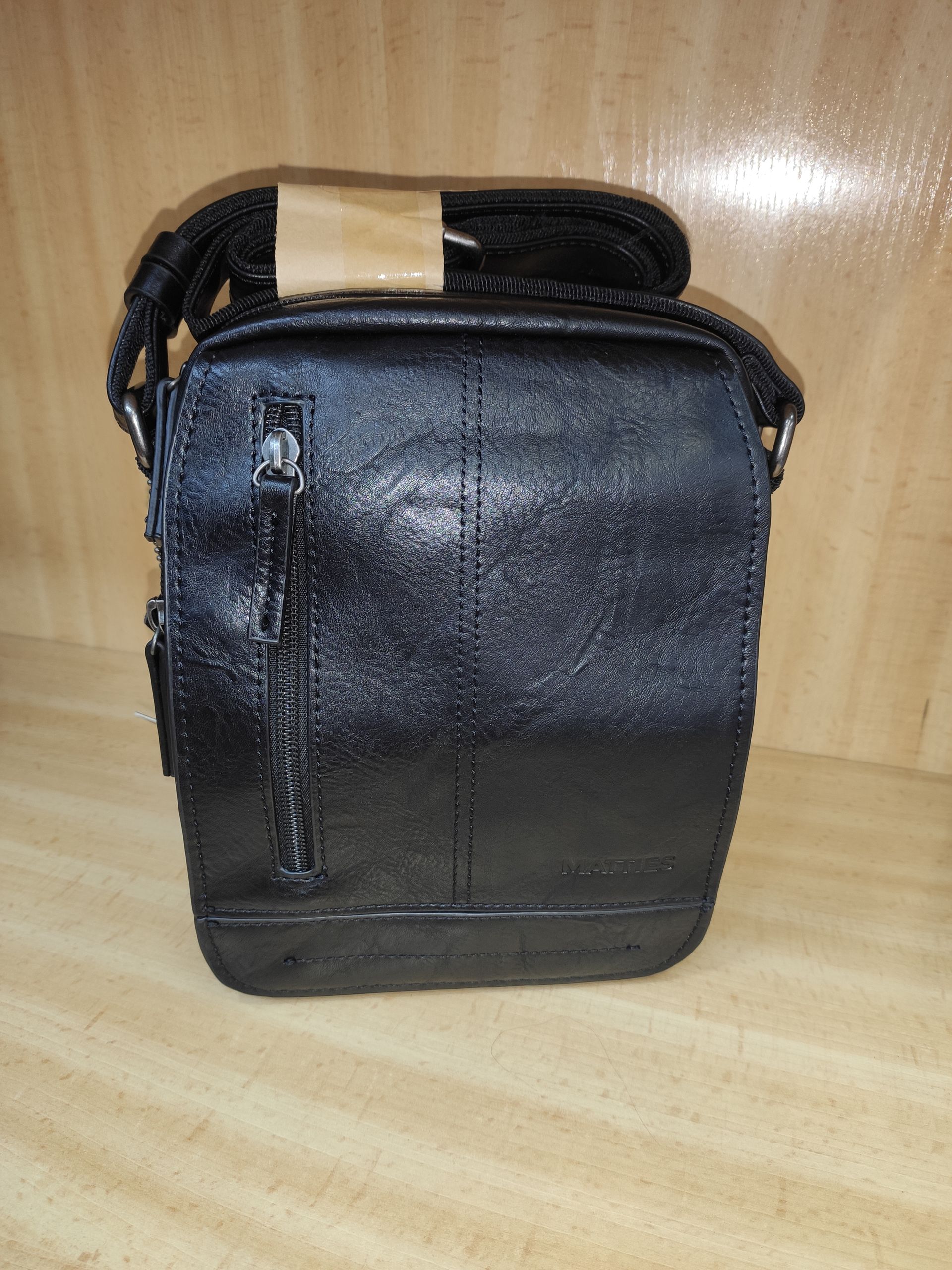 Un bolso de mensajero de cuero negro está sobre una mesa de madera.