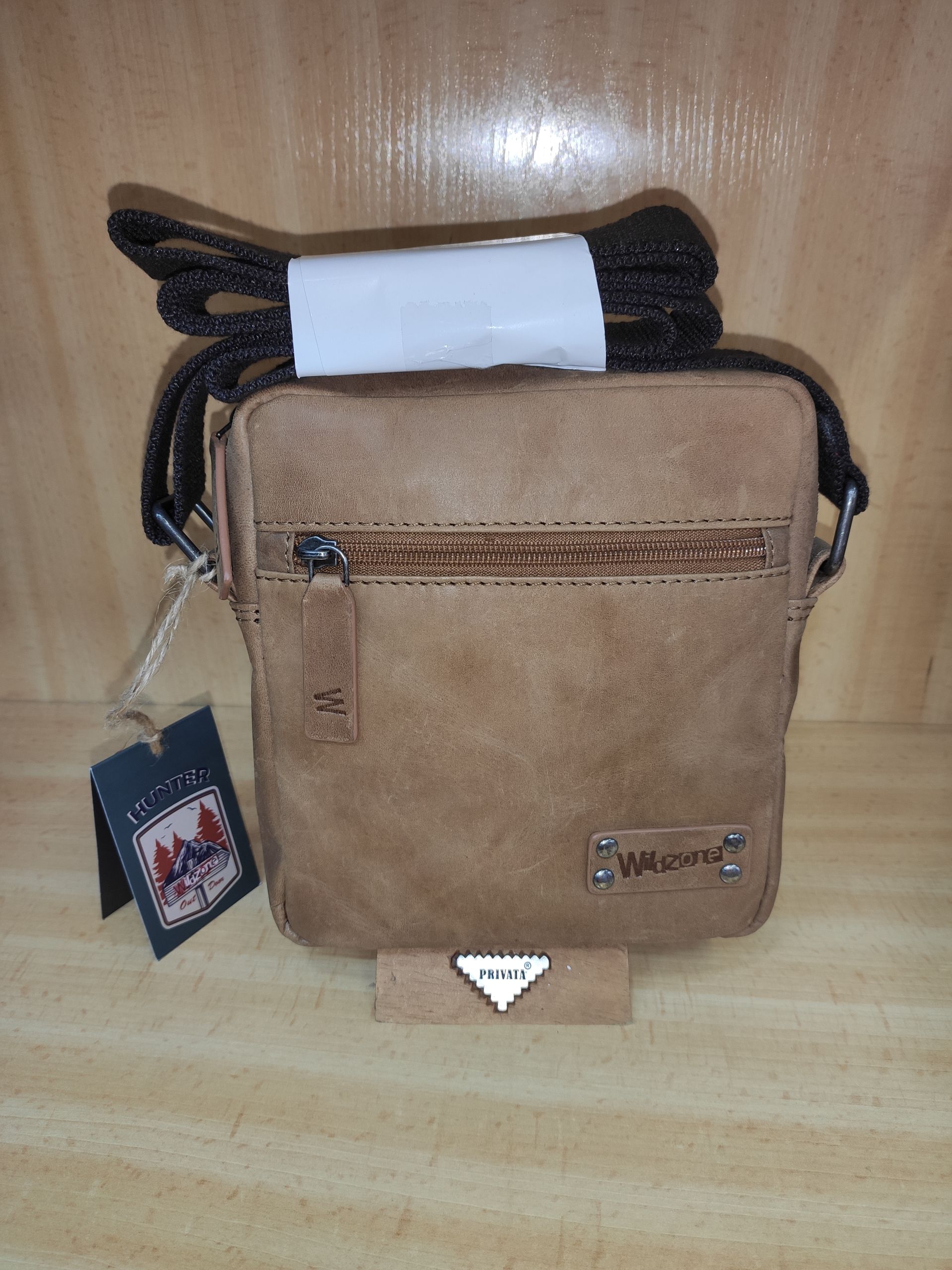 Un bolso de mensajero marrón con una correa negra está sobre una mesa de madera.