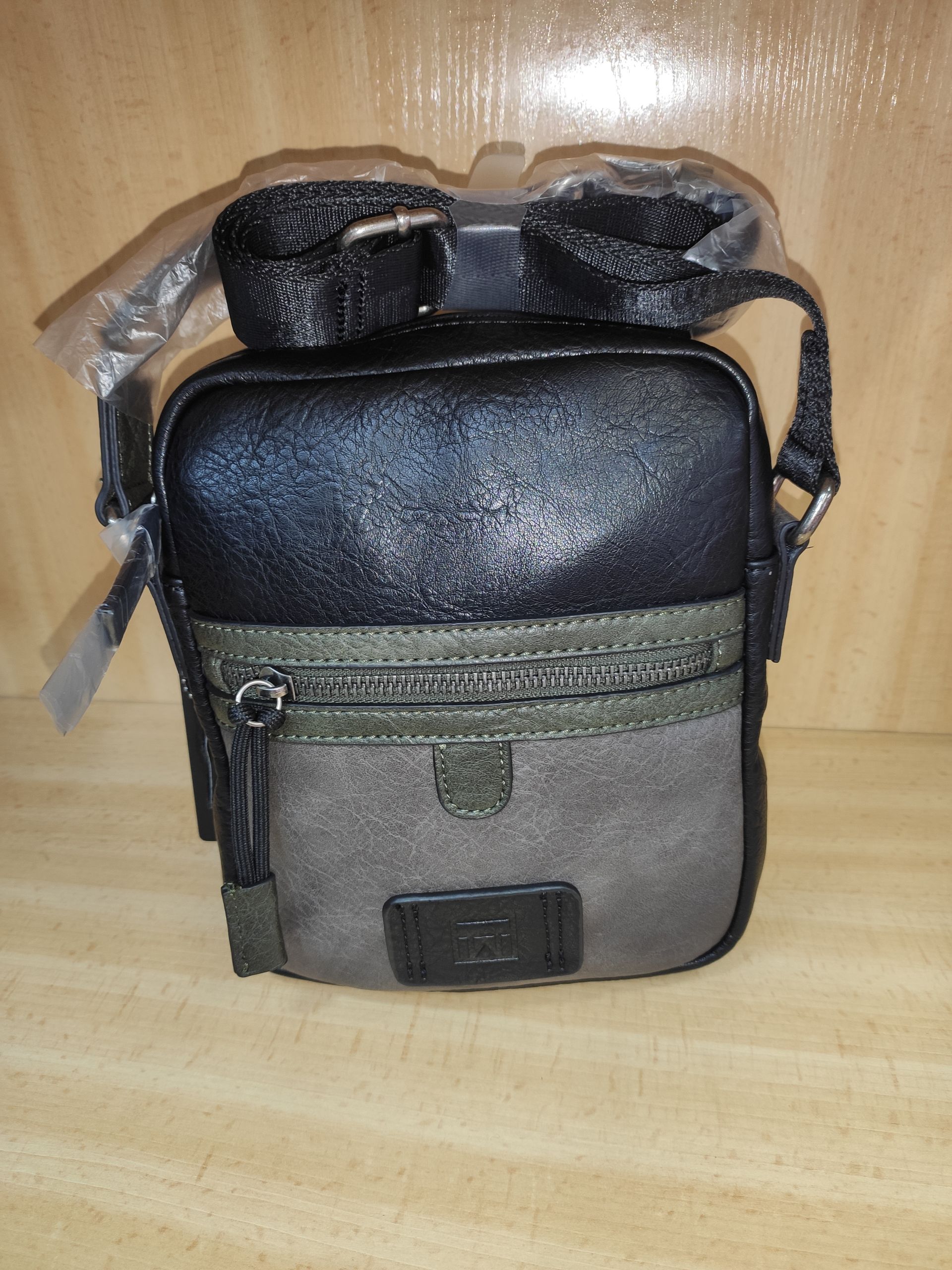 Un pequeño bolso negro y gris con una correa está sobre una mesa de madera.