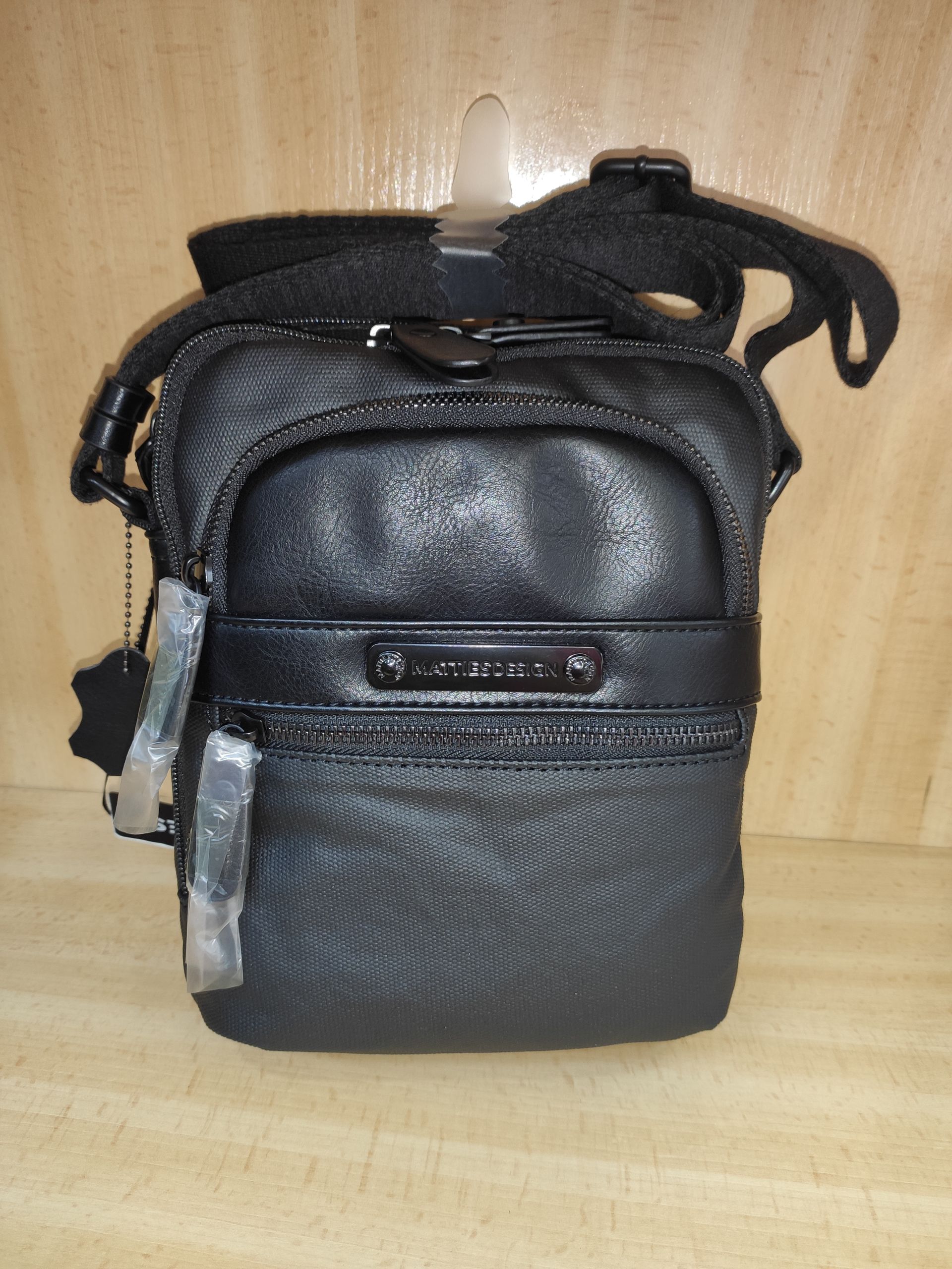 Un pequeño bolso negro con una correa está sobre una mesa de madera.