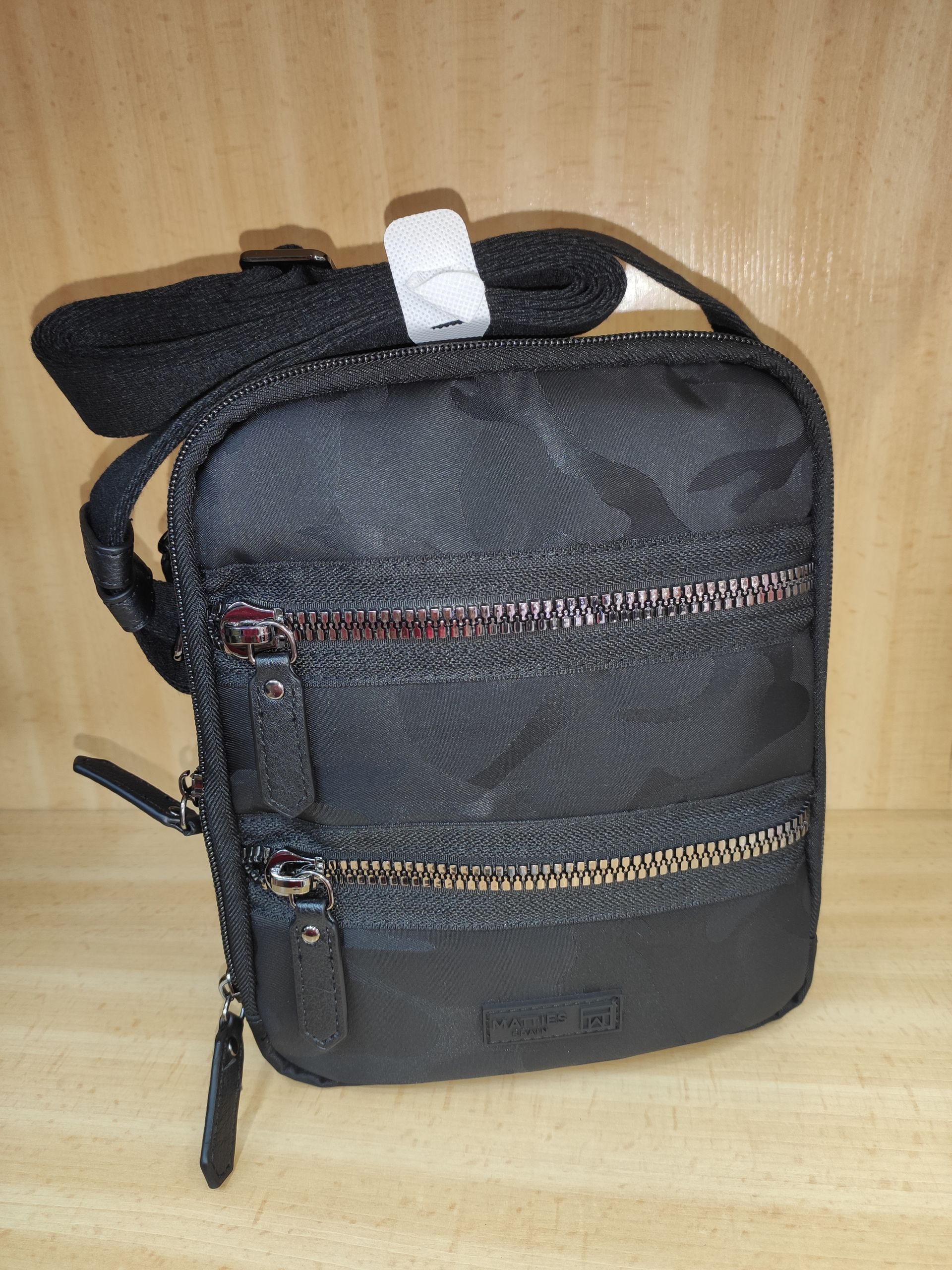 Un pequeño bolso negro con una correa está sobre una mesa de madera.