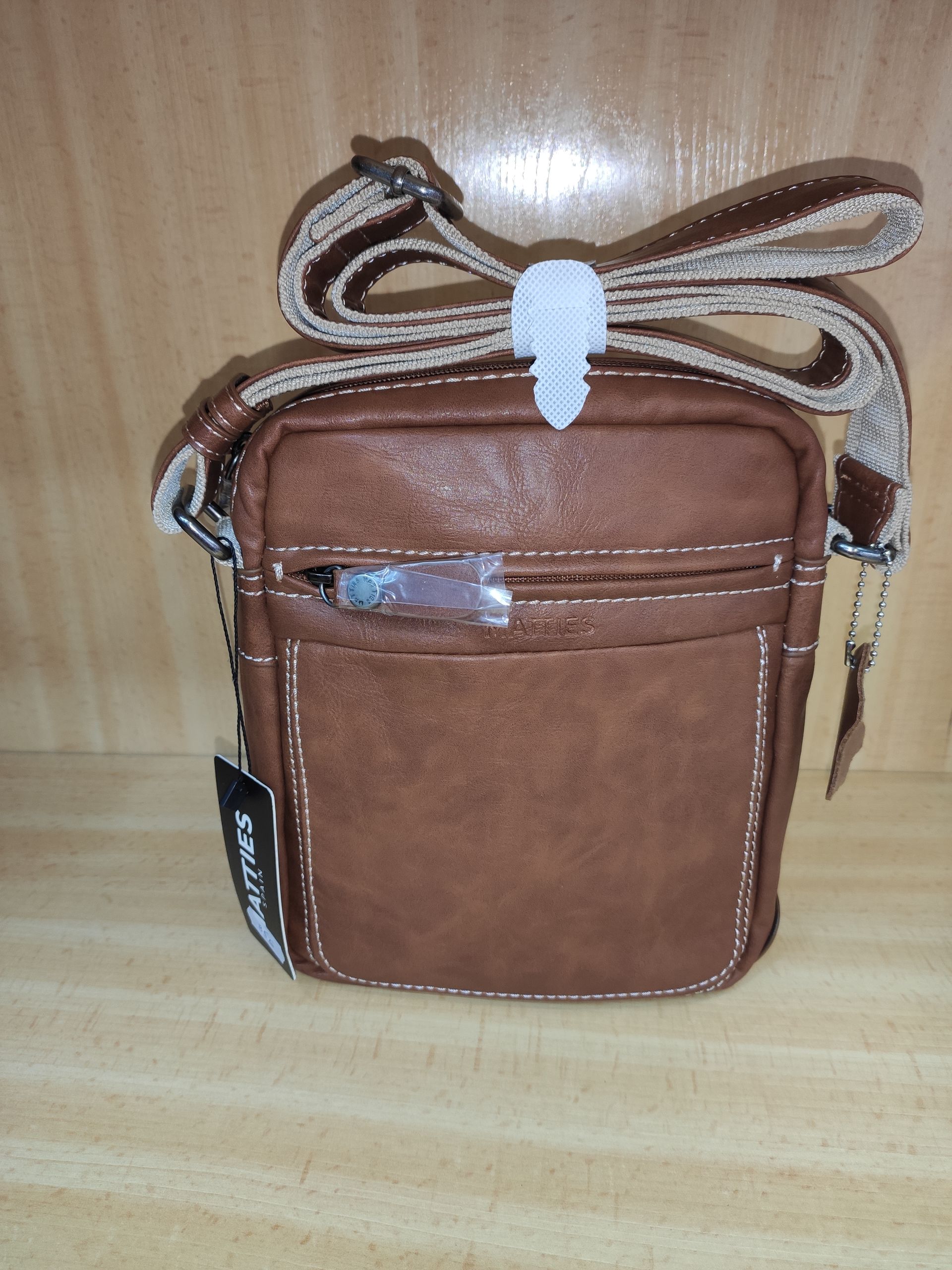 Un bolso marrón con una correa está sobre una mesa de madera.