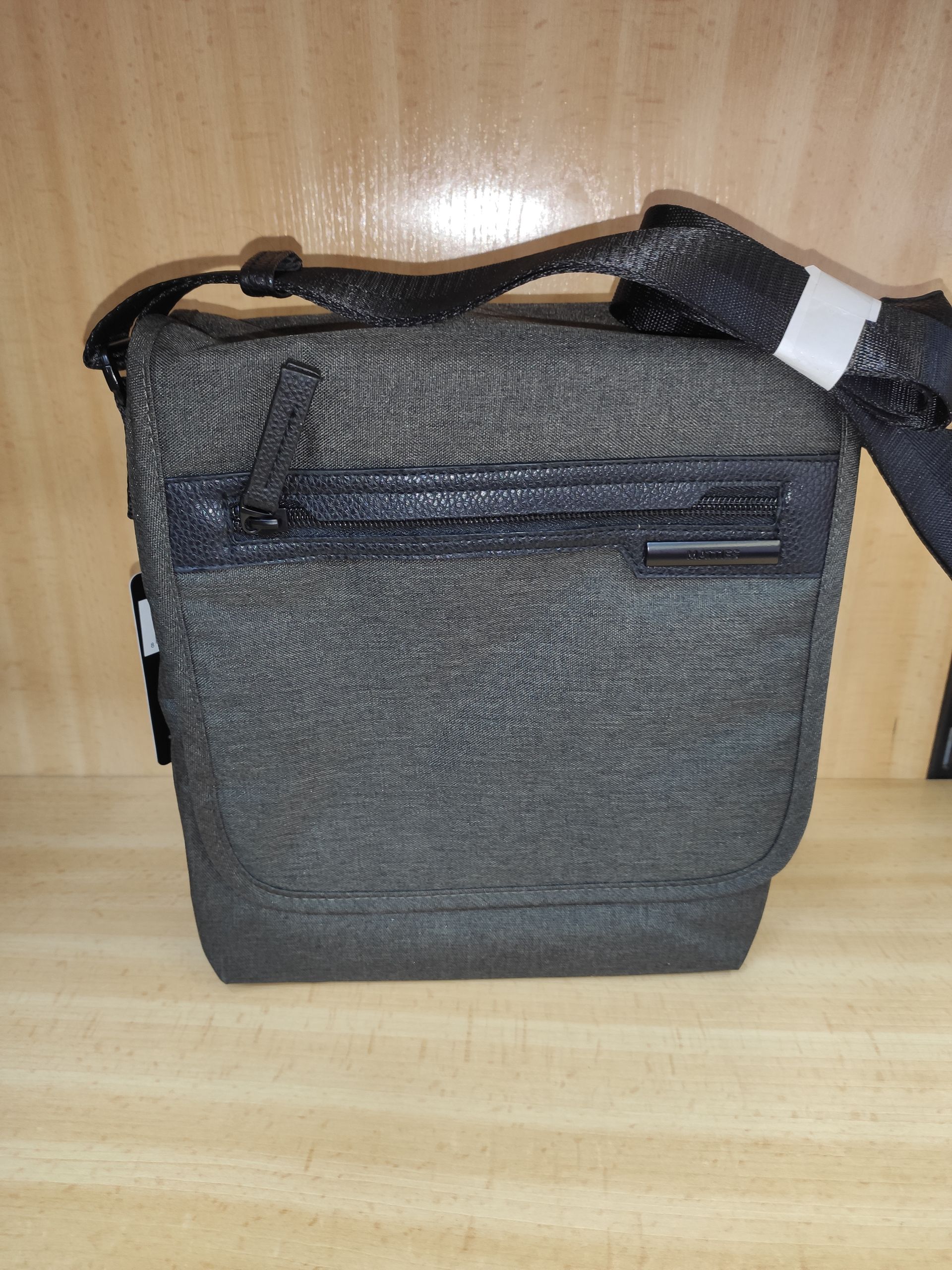 Un bolso de mensajero negro está sobre una mesa de madera.