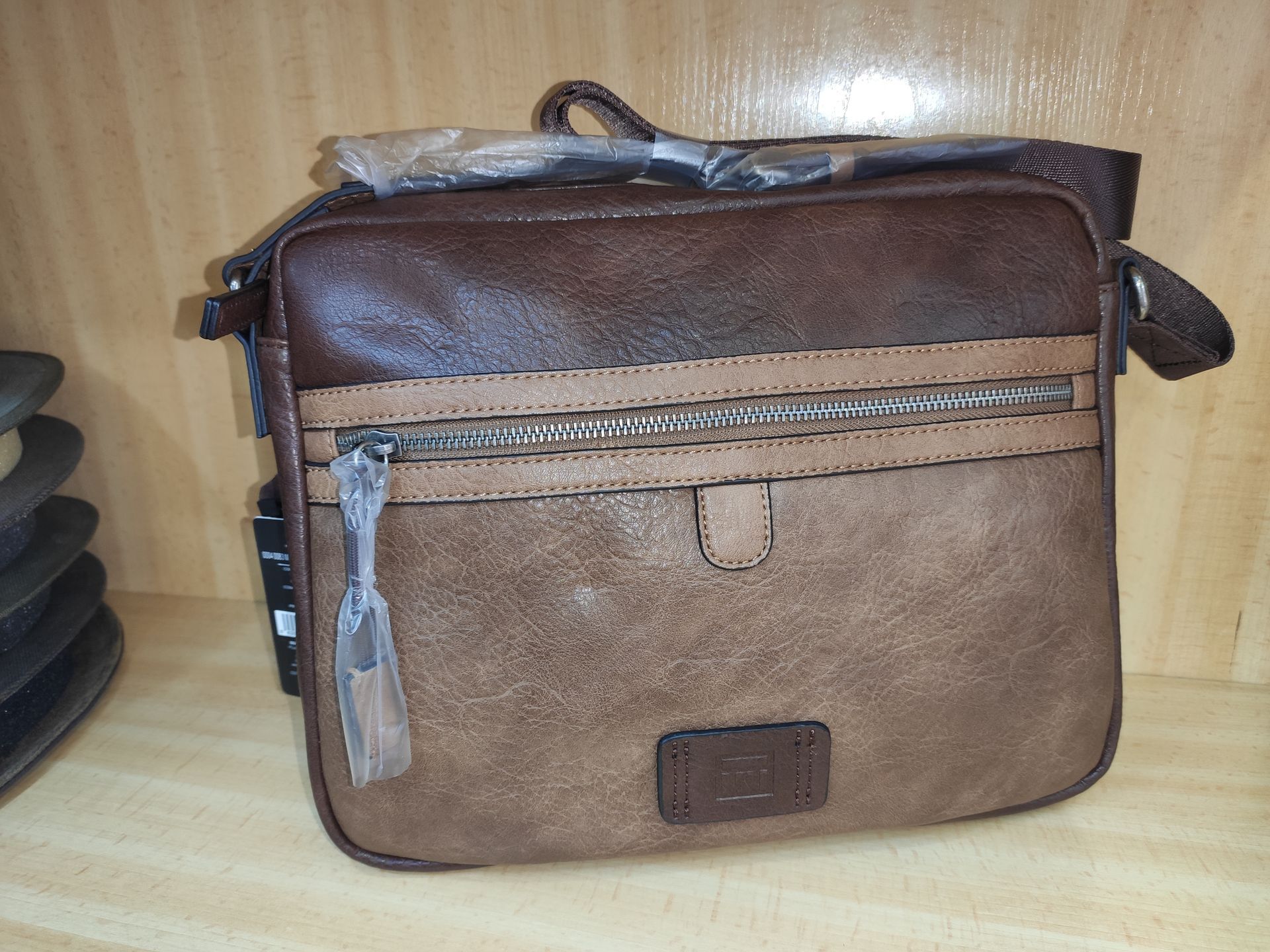 Un bolso mensajero de cuero marrón con cremallera en la parte delantera.