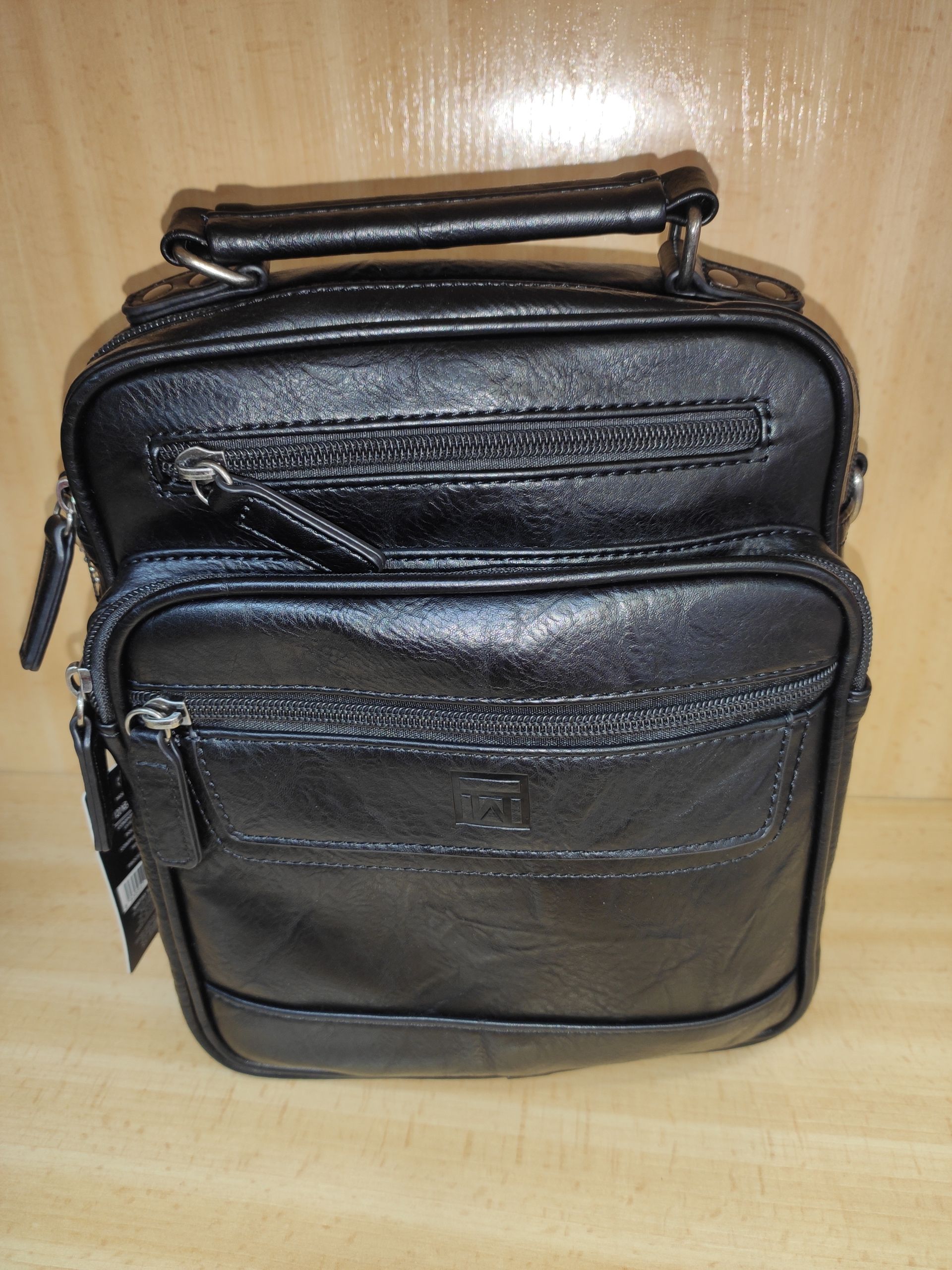 Un bolso de cuero negro con asa está sobre una mesa de madera.