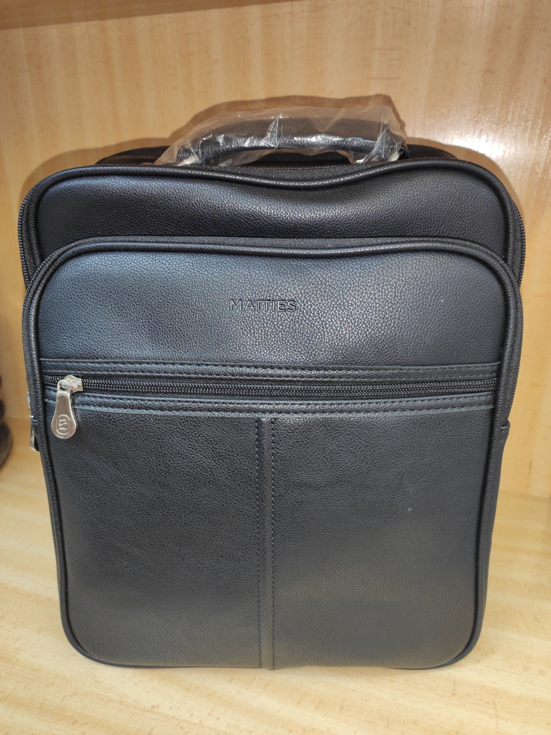 Una bolsa negra con asa está sobre un estante de madera.