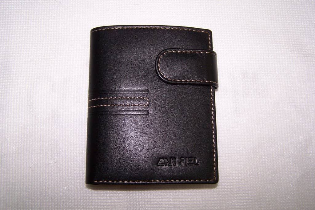 Una billetera de cuero negra con costuras blancas reposa sobre una superficie blanca.