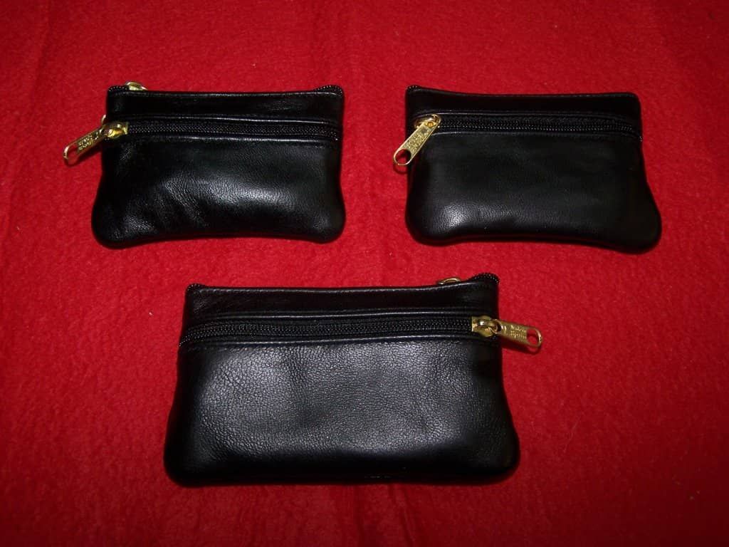 Tres carteras de cuero negro con tiradores de cremallera dorados sobre una tela roja