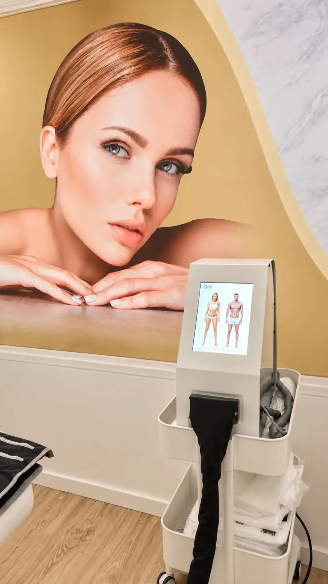 Clinic room with a facial treatment device and a large wall poster of a woman’s face