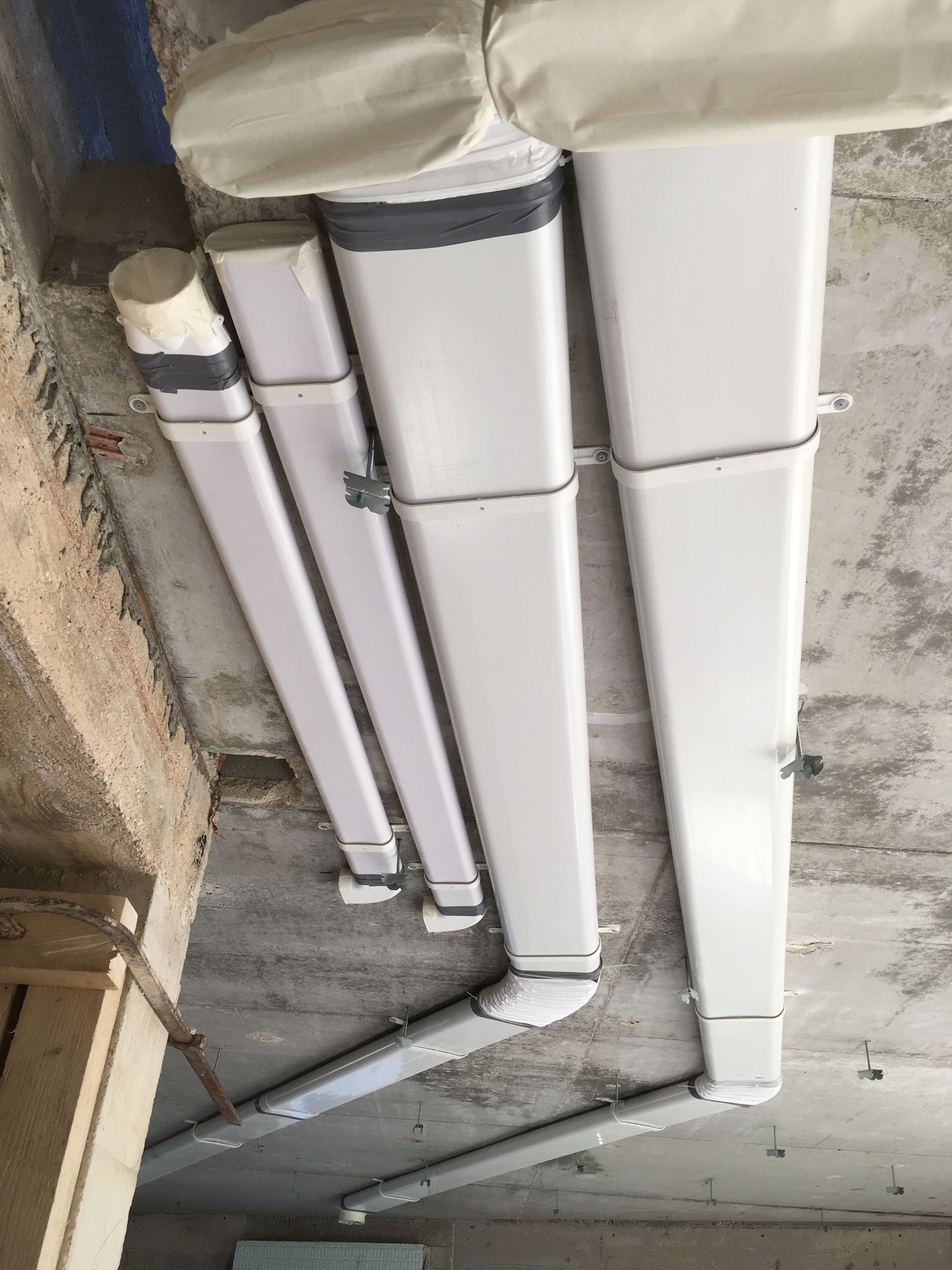 Tubes de plomberie en plastique blanc fixés au mur avec des attaches métalliques.