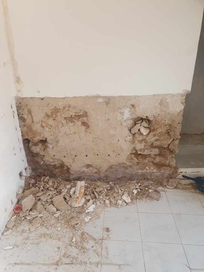 Un mur intérieur endommagé avec des morceaux de plâtre et de béton tombés au sol.