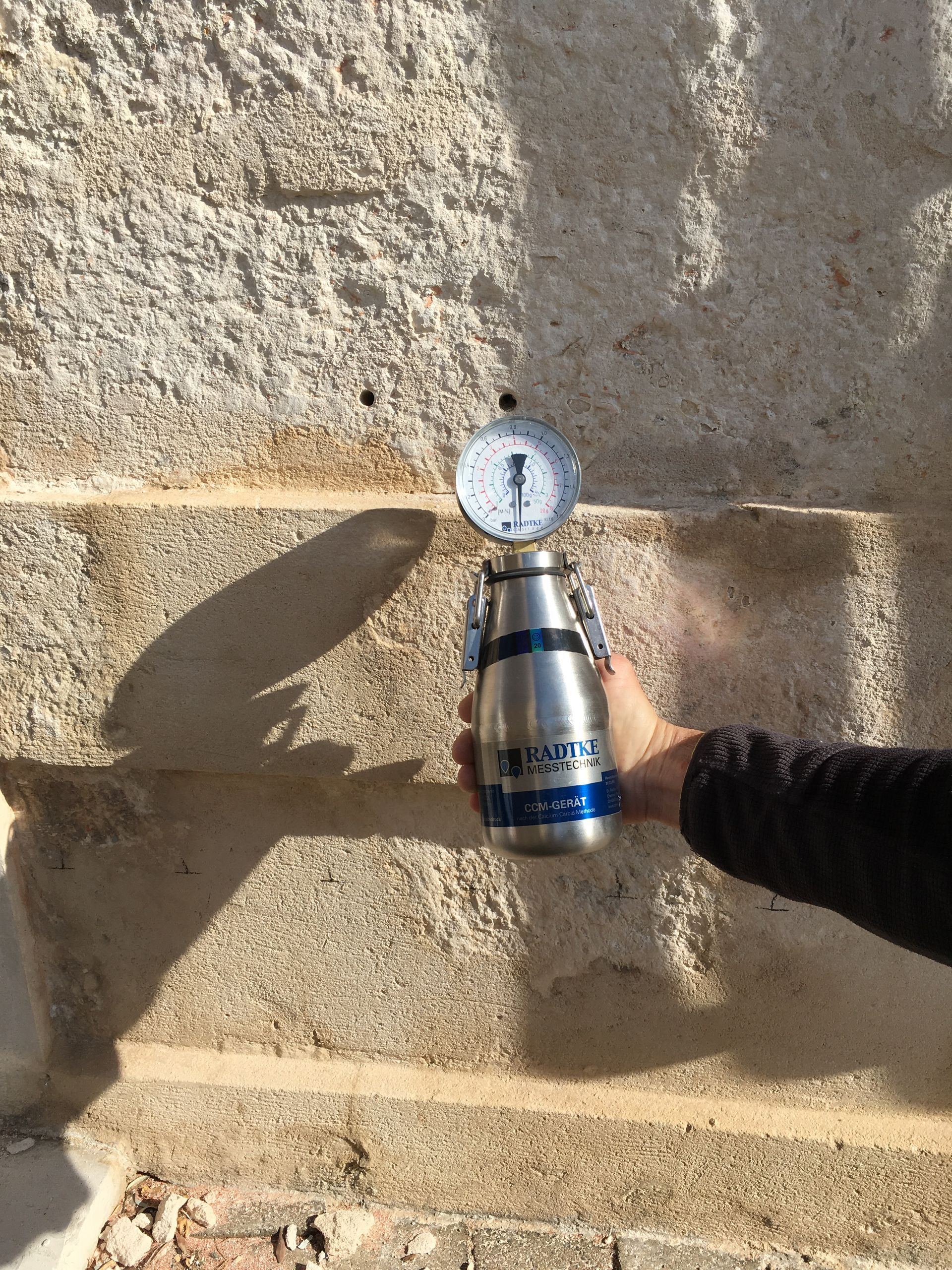 Un manomètre analogique connecté à un cylindre métallique inséré dans un trou de forage dans un mur.