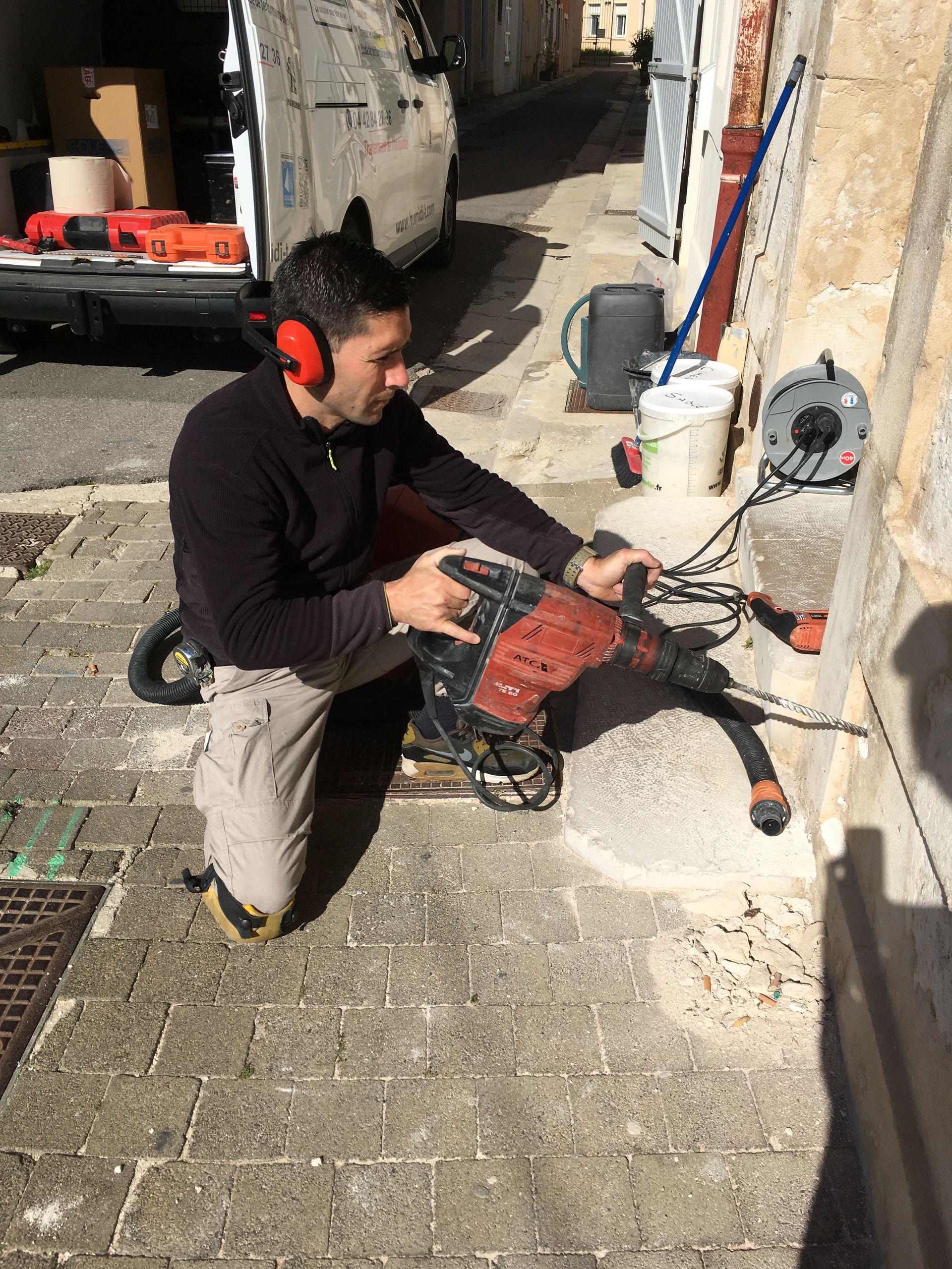 Un homme en train de percer des trous dans un mur en béton avec une perceuse électrique.