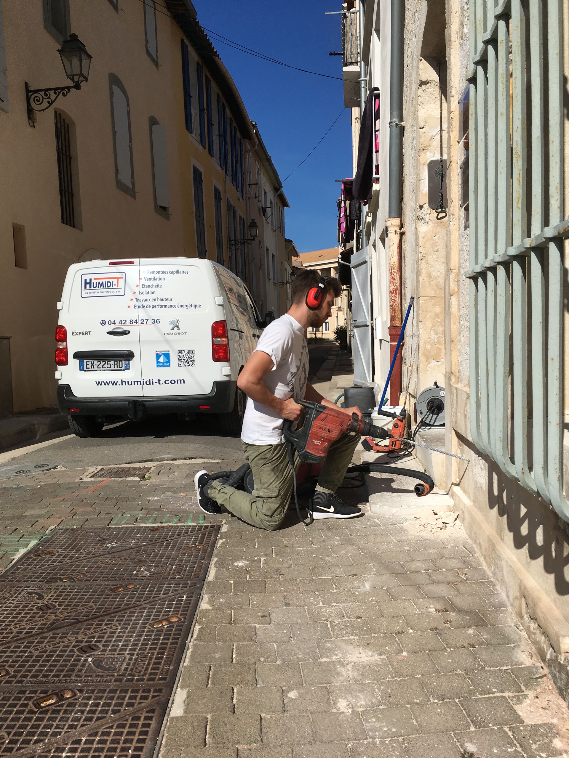 Un homme debout à côté d'un véhicule utilitaire blanc, tenant une perceuse électrique.