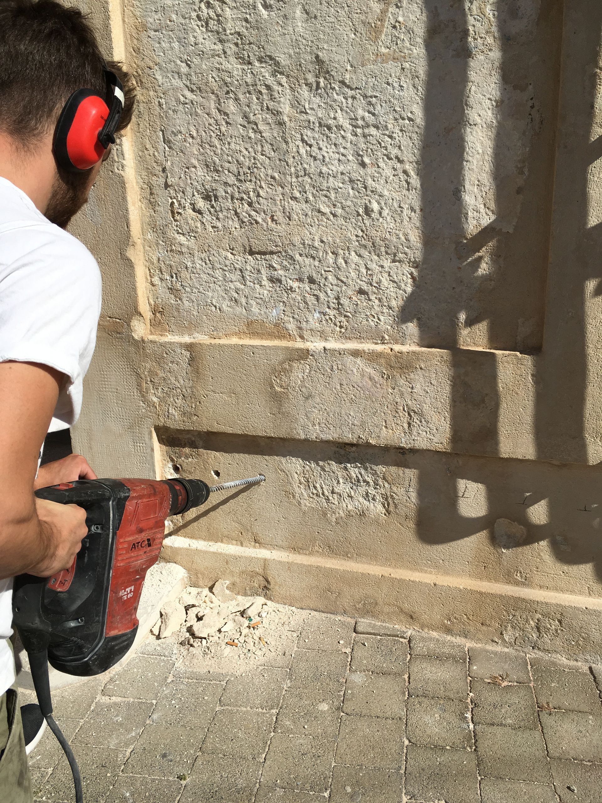 Un homme en train de percer un mur en pierre avec une perceuse électrique, vue de près.
