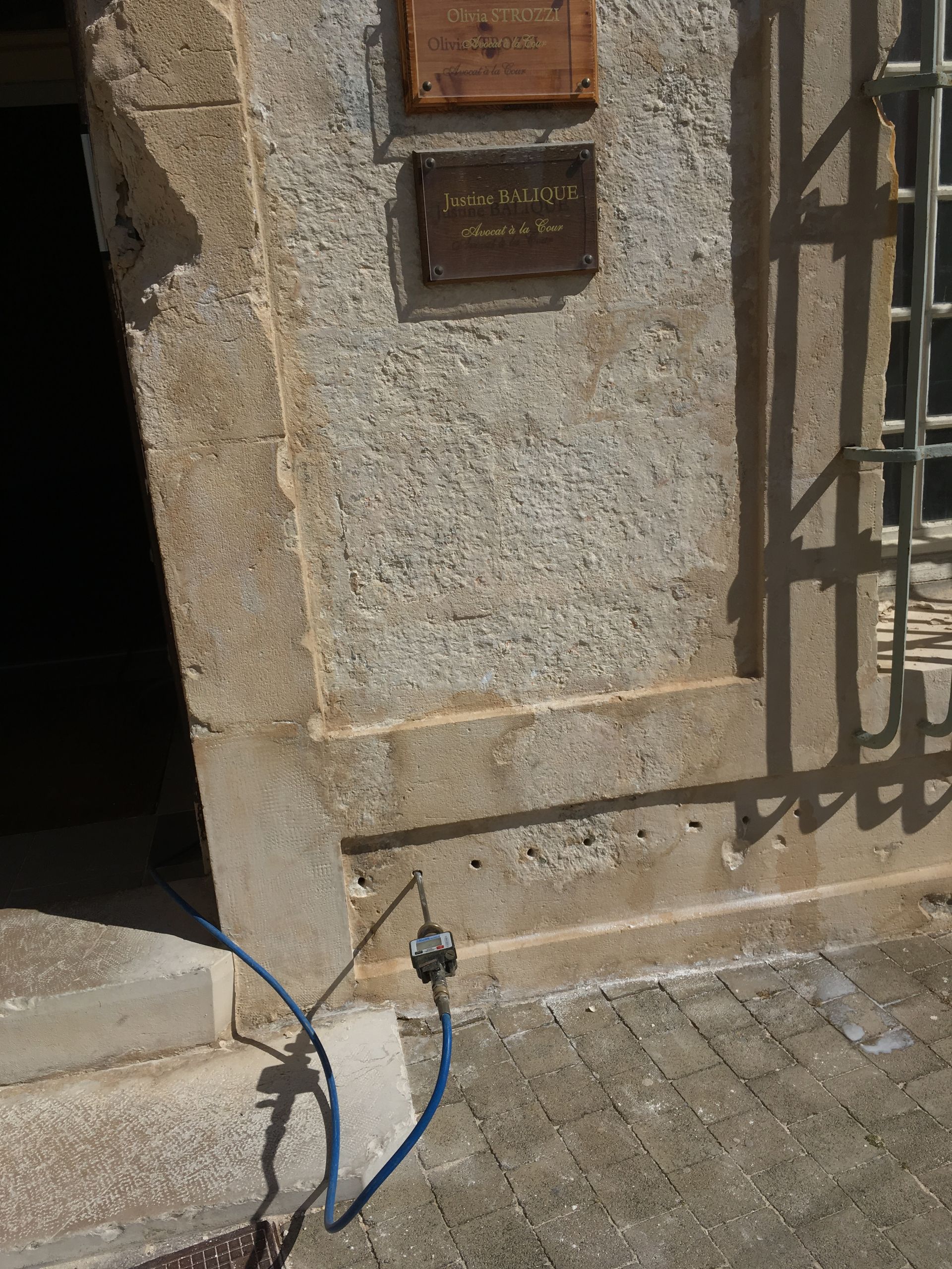 Deux plaques commémoratives fixées sur un mur en pierre, avec un câble électrique bleu à proximité.