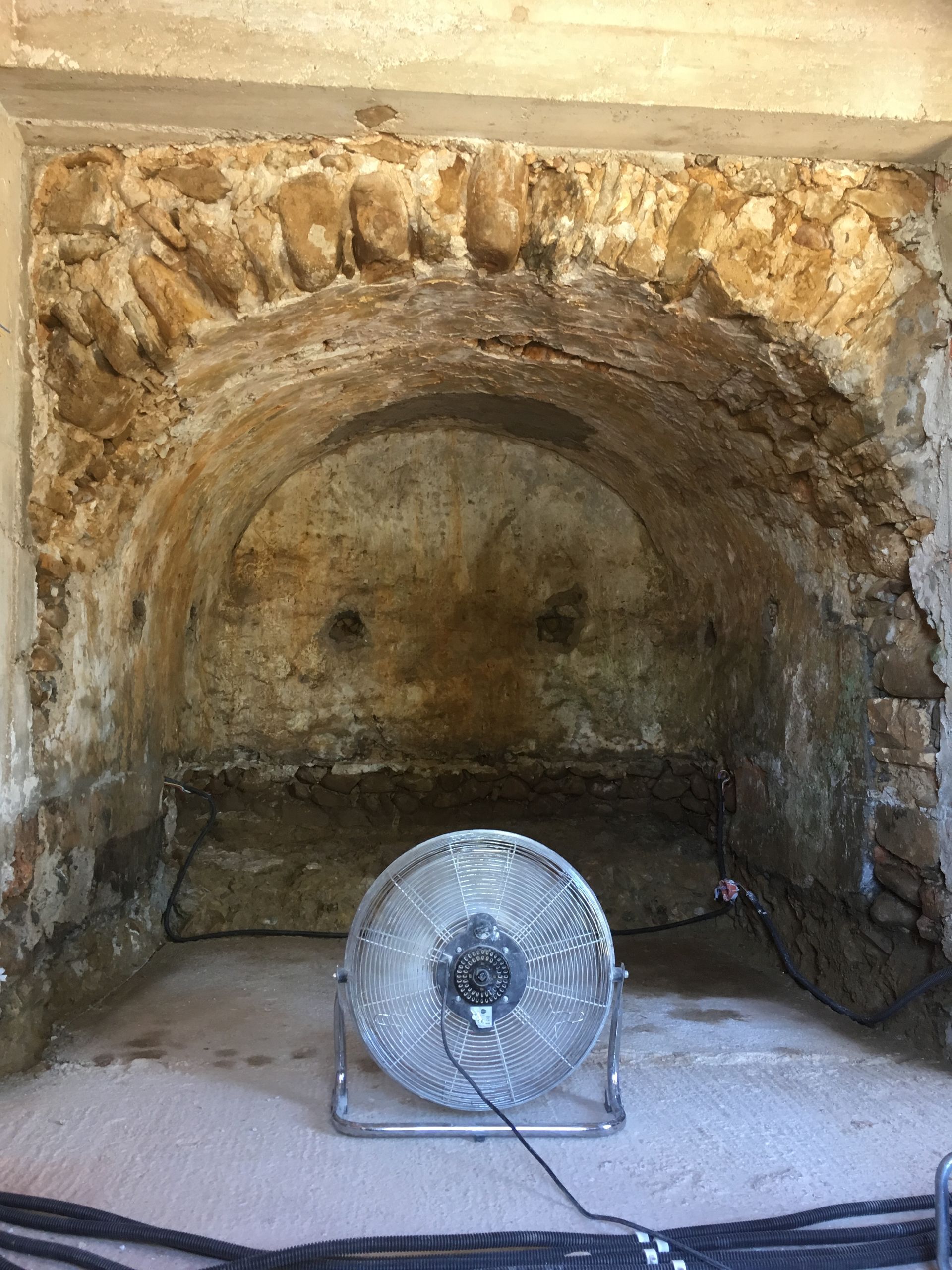 Vue d'un puits ou d'une cavité en pierre avec un ventilateur posé à côté.