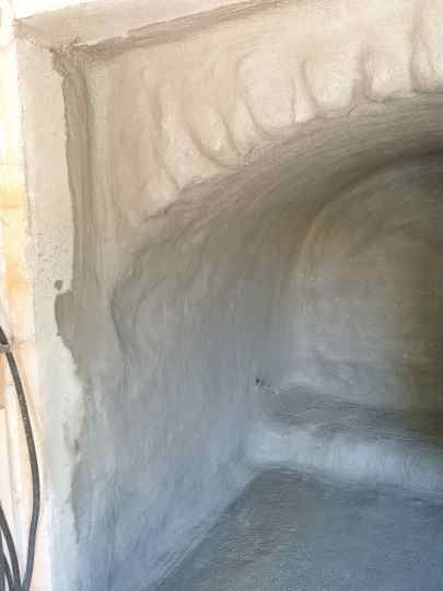 Un mur en plâtre avec une arche en demi-cercle. Le plâtre est fraîchement appliqué et encore humide, avec des traces visibles de l'application.