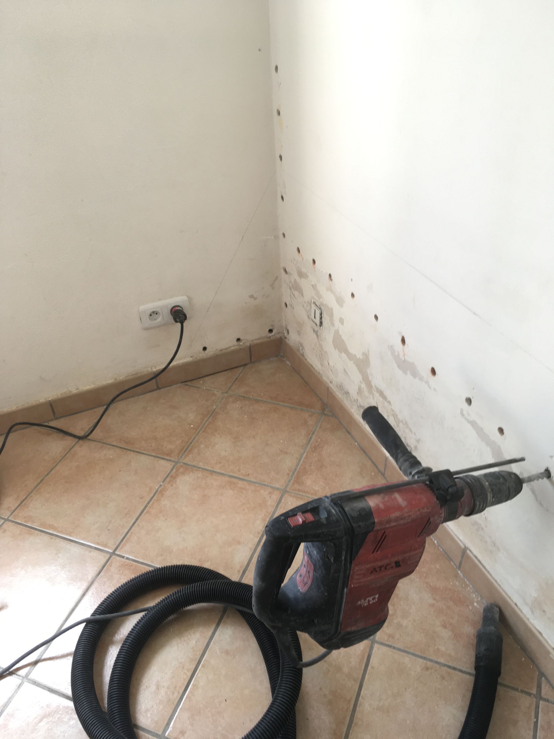 Perforateur électrique perçant un trou dans un mur avec des signes de moisissure.