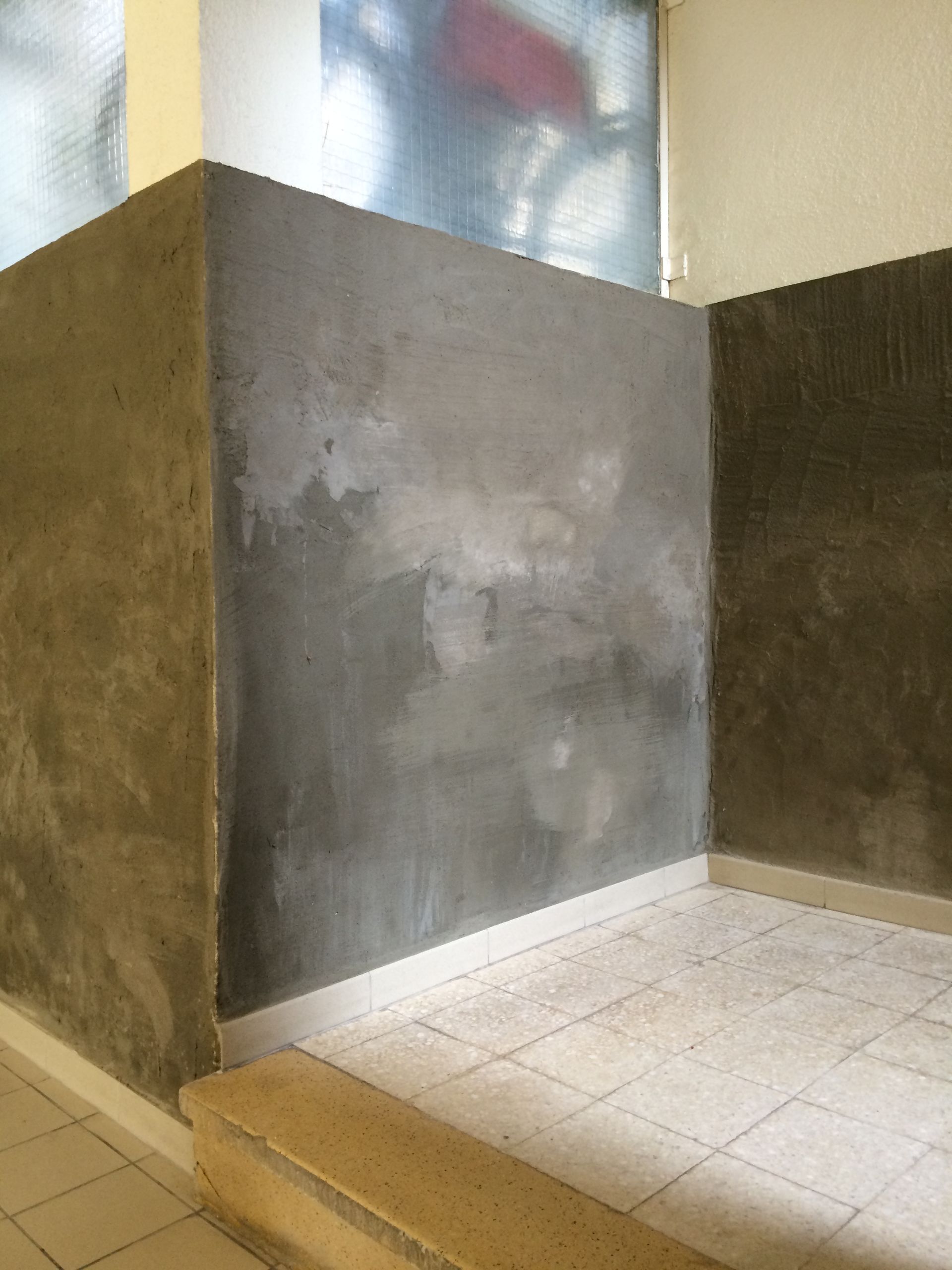 Coin de mur intérieur avec une couche de plâtre gris appliquée de manière inégale.